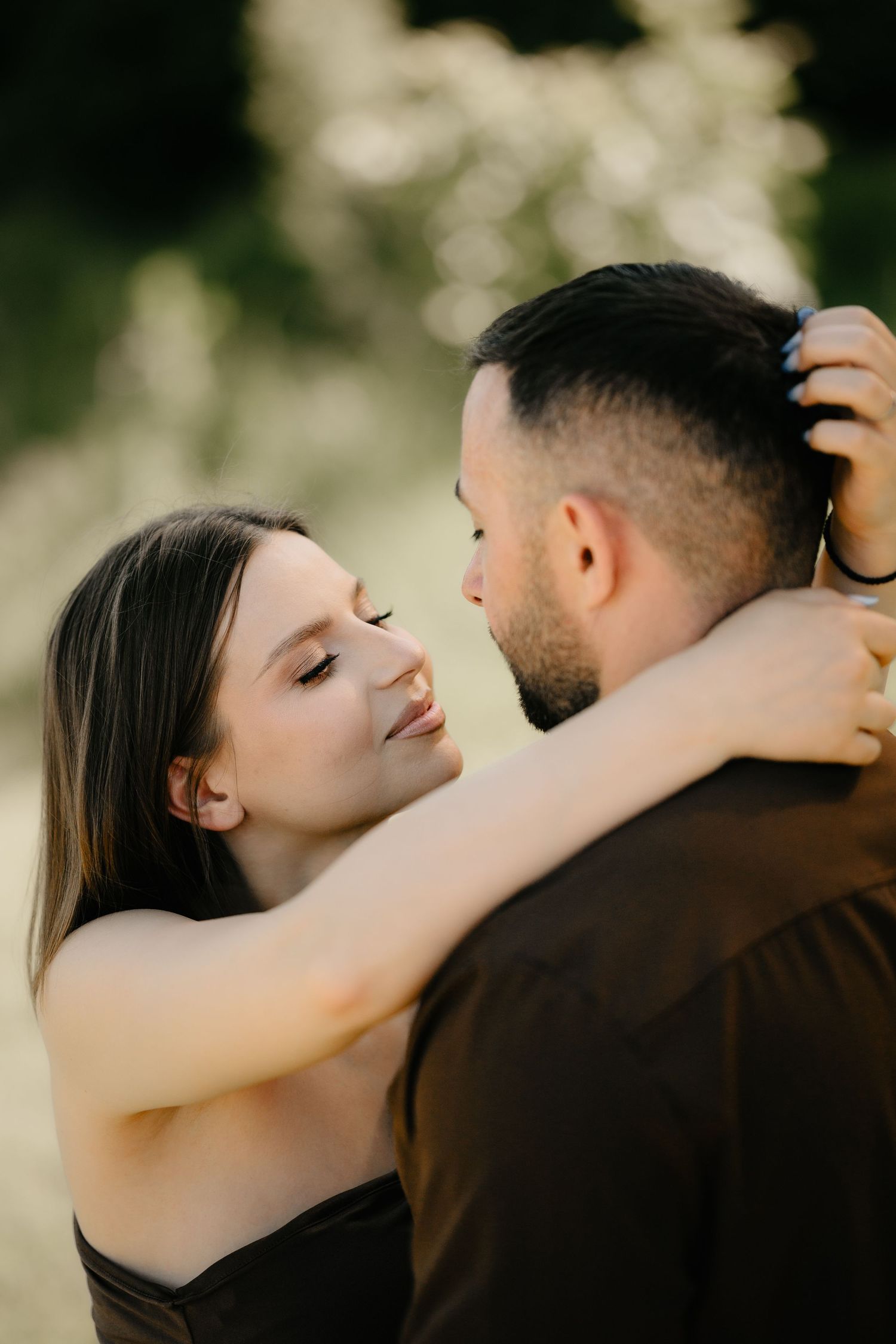 Romantic couple embracing in nature, woman smiling lovingly at bearded man in dark shirt.