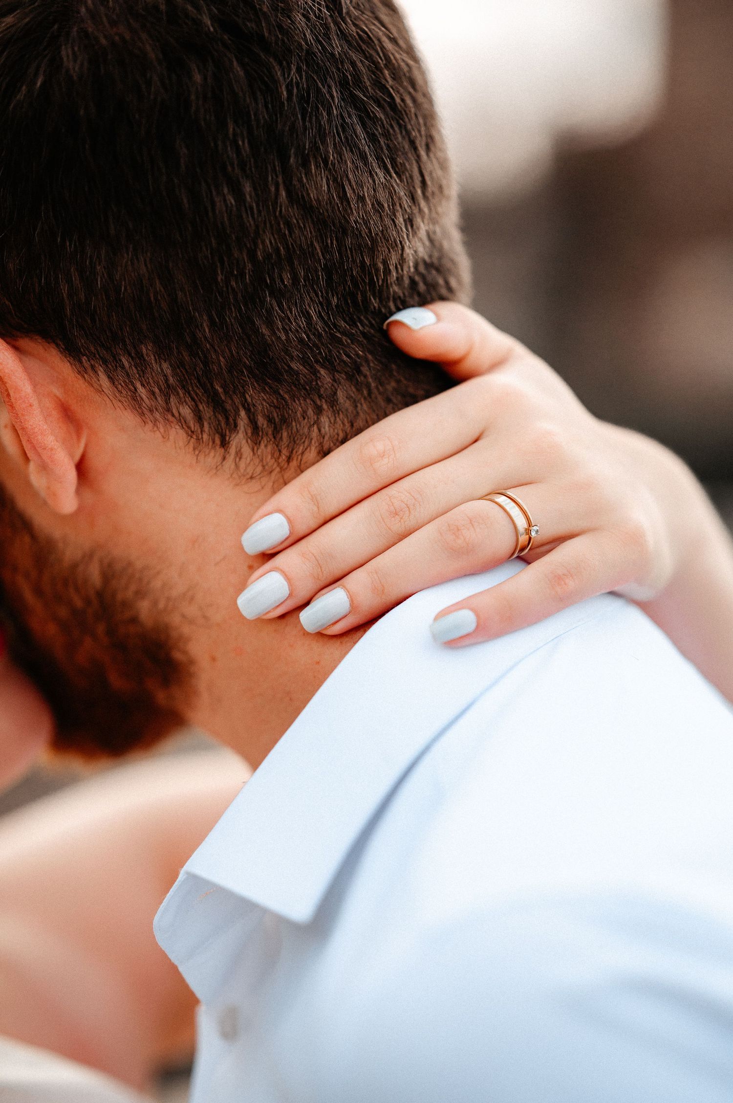 Close-up of bride's hand with gold wedding ring resting on groom's neck in white shirt.