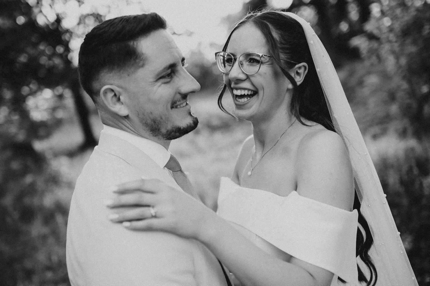 Black and white portrait of laughing bride and groom embracing outdoors on their wedding day.