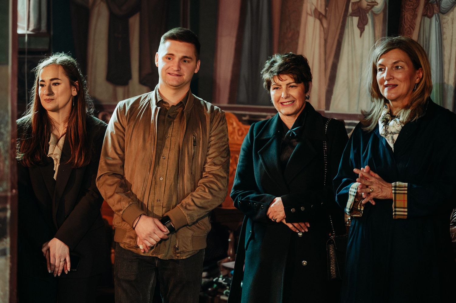 Family group of four posing together inside an ornate Orthodox church during a baptism.