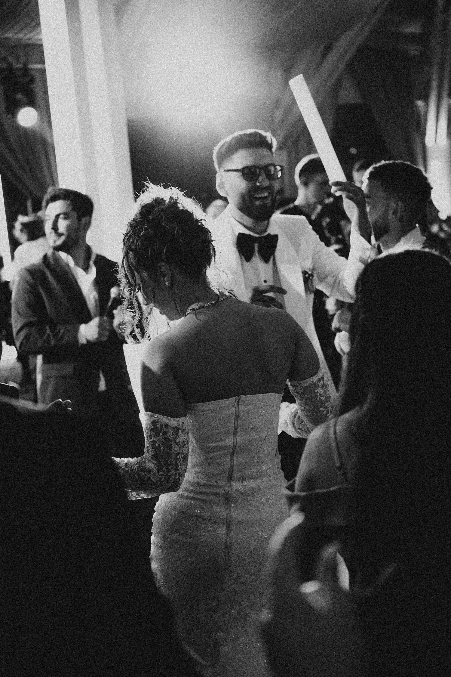 Black and white photo of bride and groom dancing at wedding reception surrounded by guests.