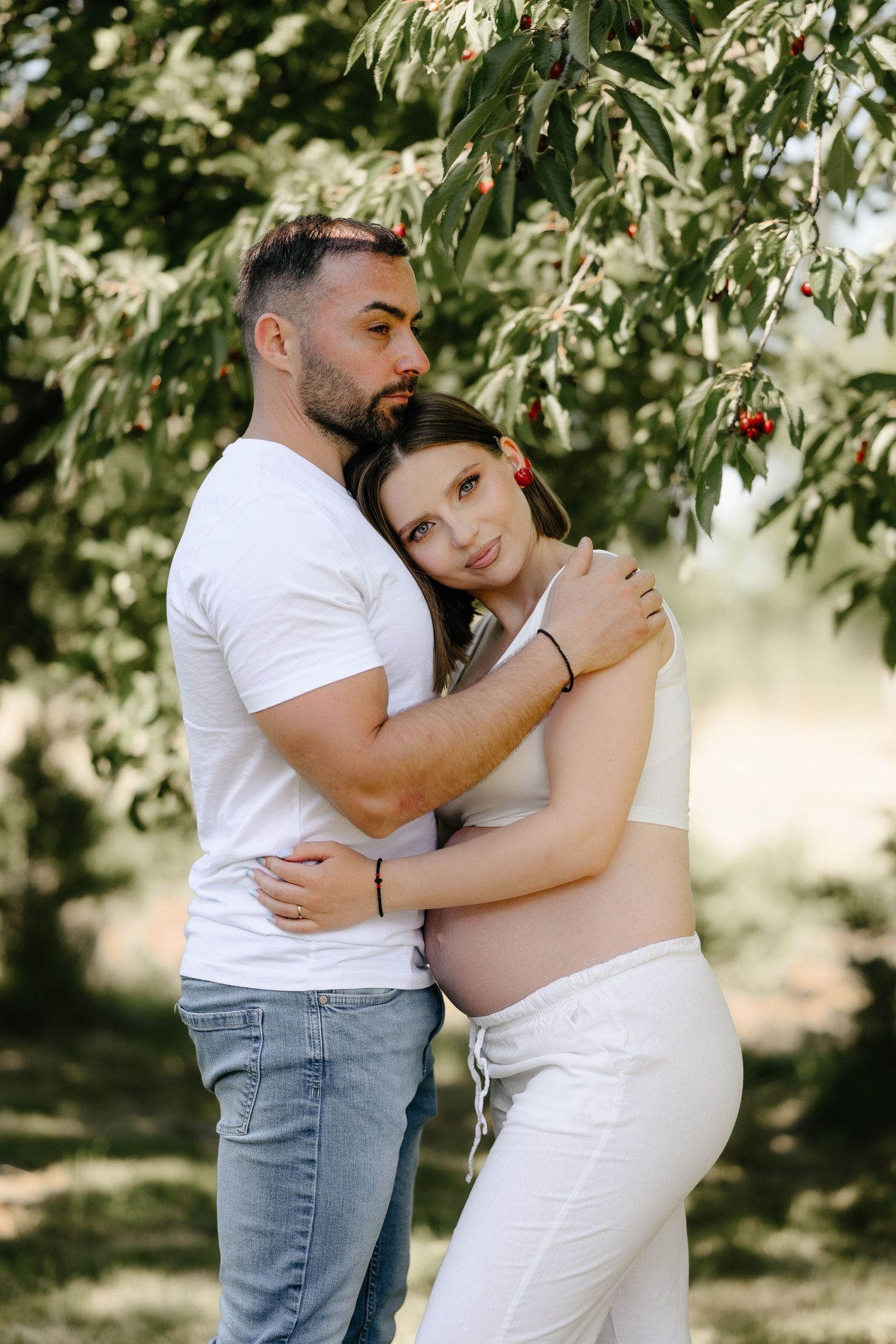 Pregnant couple embracing tenderly under a cherry tree outdoors.