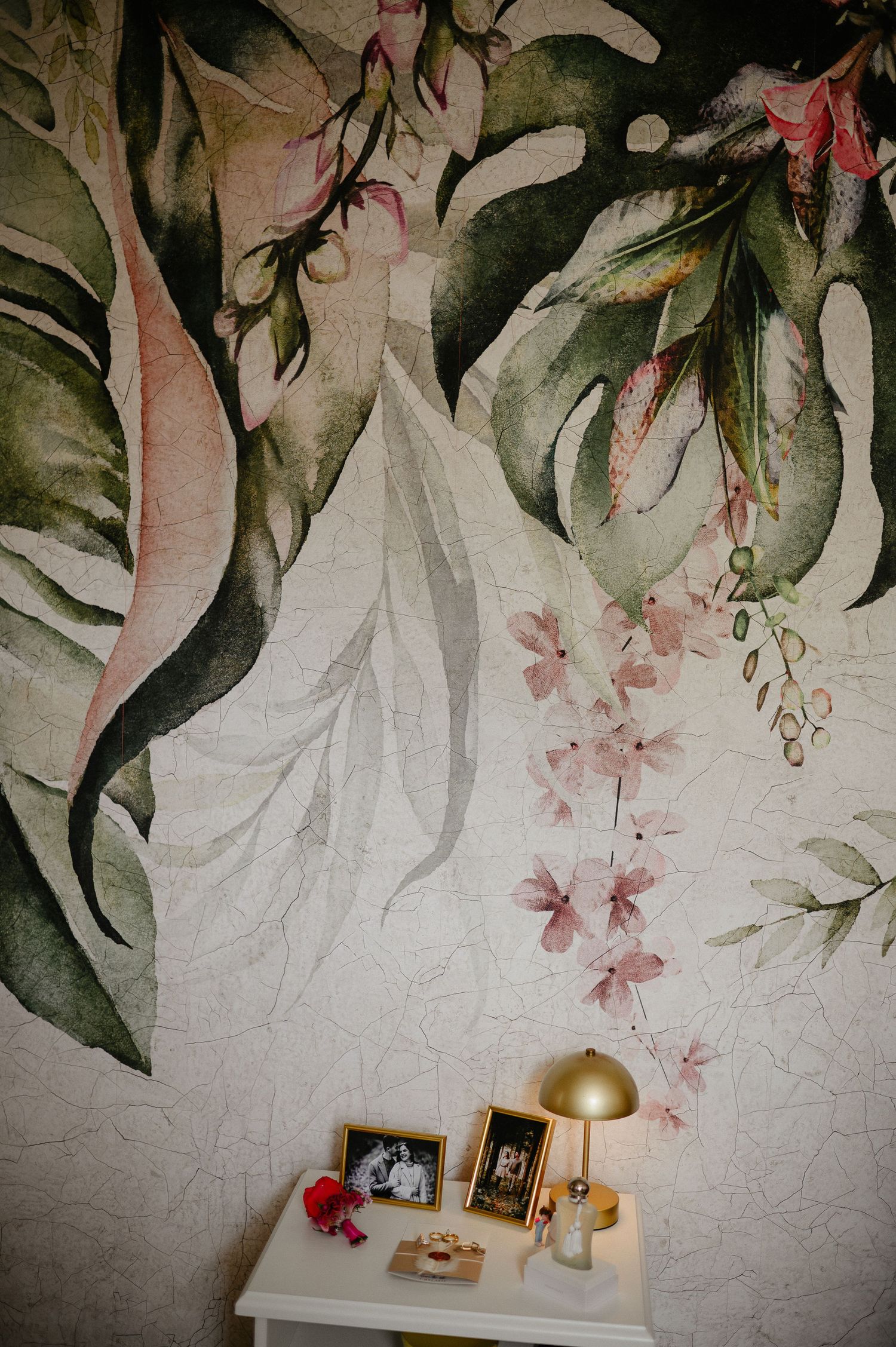 Elegant floral wall mural above white nightstand with framed wedding photos and gold lamp decor.