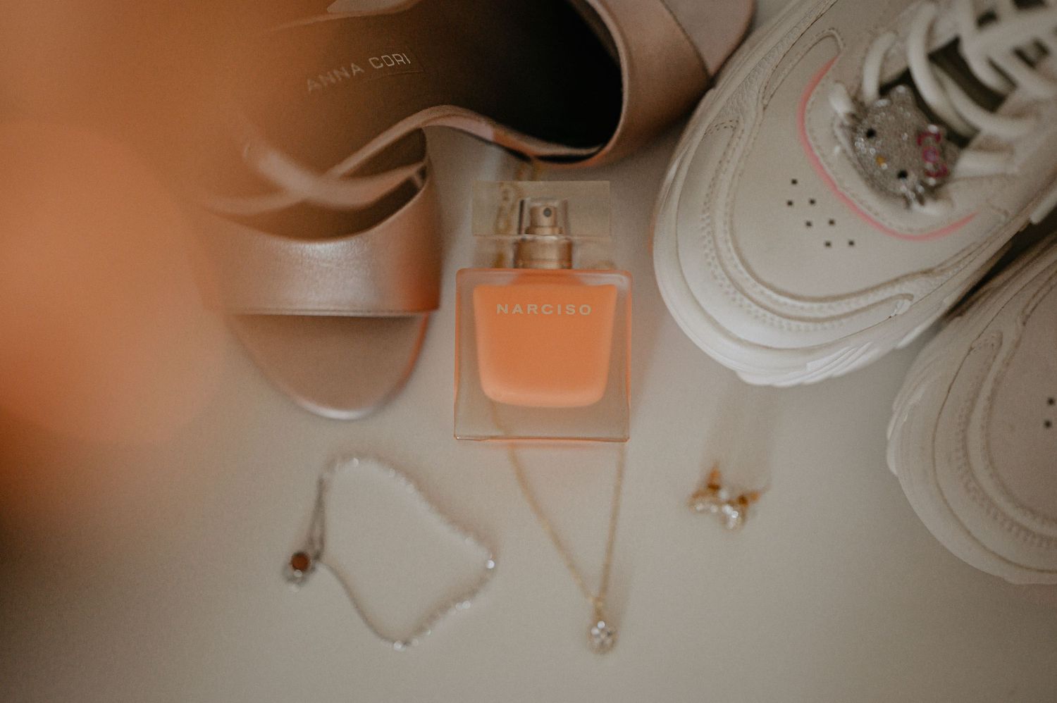 Flat lay of wedding accessories including heels, sneakers, perfume, bracelet, and earrings in peach tones.