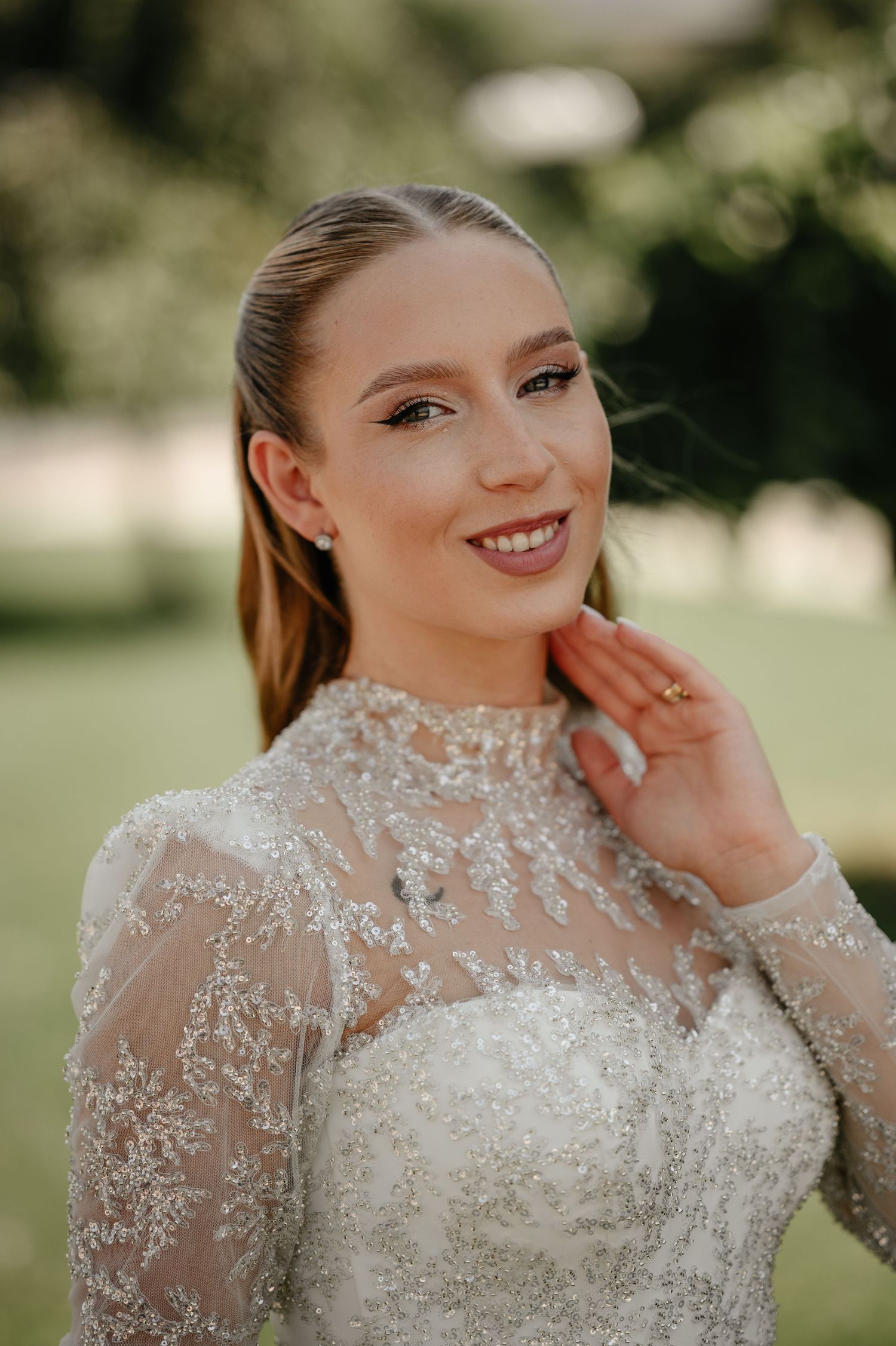 Smiling bride in beaded high-neck lace wedding dress with natural makeup and sleek hairstyle.