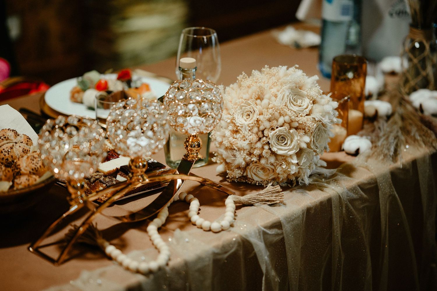 Ornate wedding head table decorated with gold candelabras and dried floral bouquet.