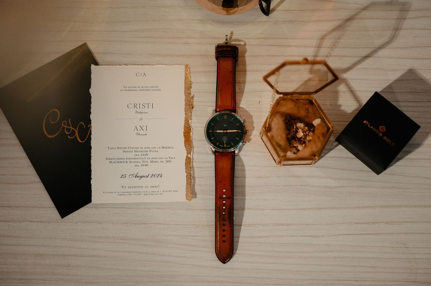 Wedding flat lay with a brown leather watch, invitation, ring box, and accessories.