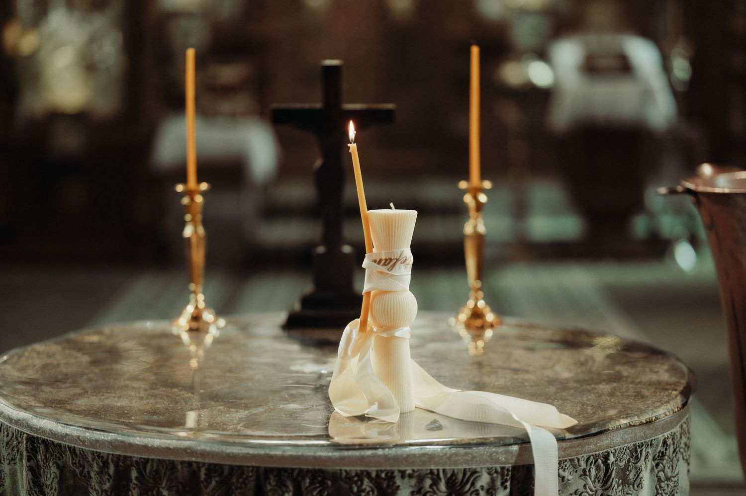 White christening candle with ribbon decoration on marble altar in church.