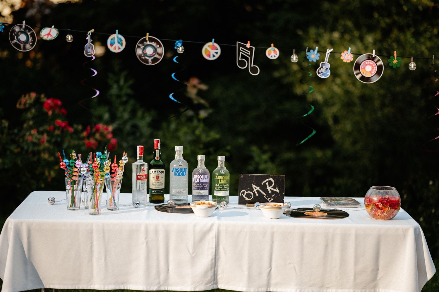 Outdoor bar table with alcohol bottles and music-themed vinyl record decorations hanging above.