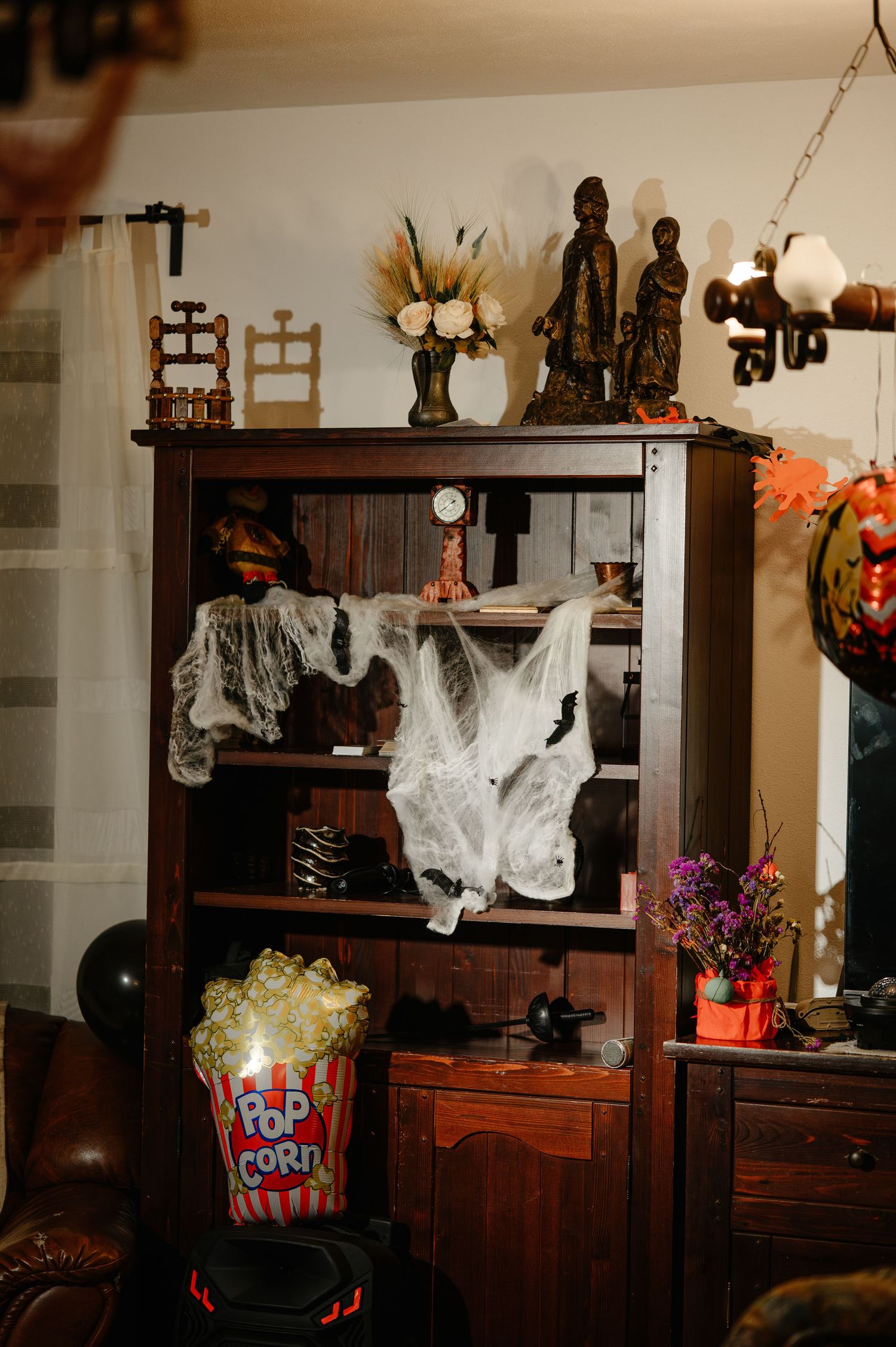 Wooden bookshelf decorated with ghost fabric and Halloween decor beside a popcorn bucket.