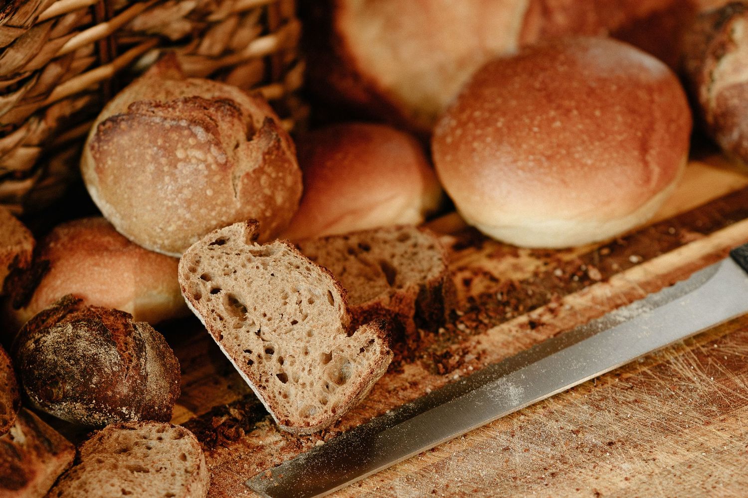 Assorted rustic artisan bread rolls and sliced sourdough loaf on a wooden cutting board with a knife.