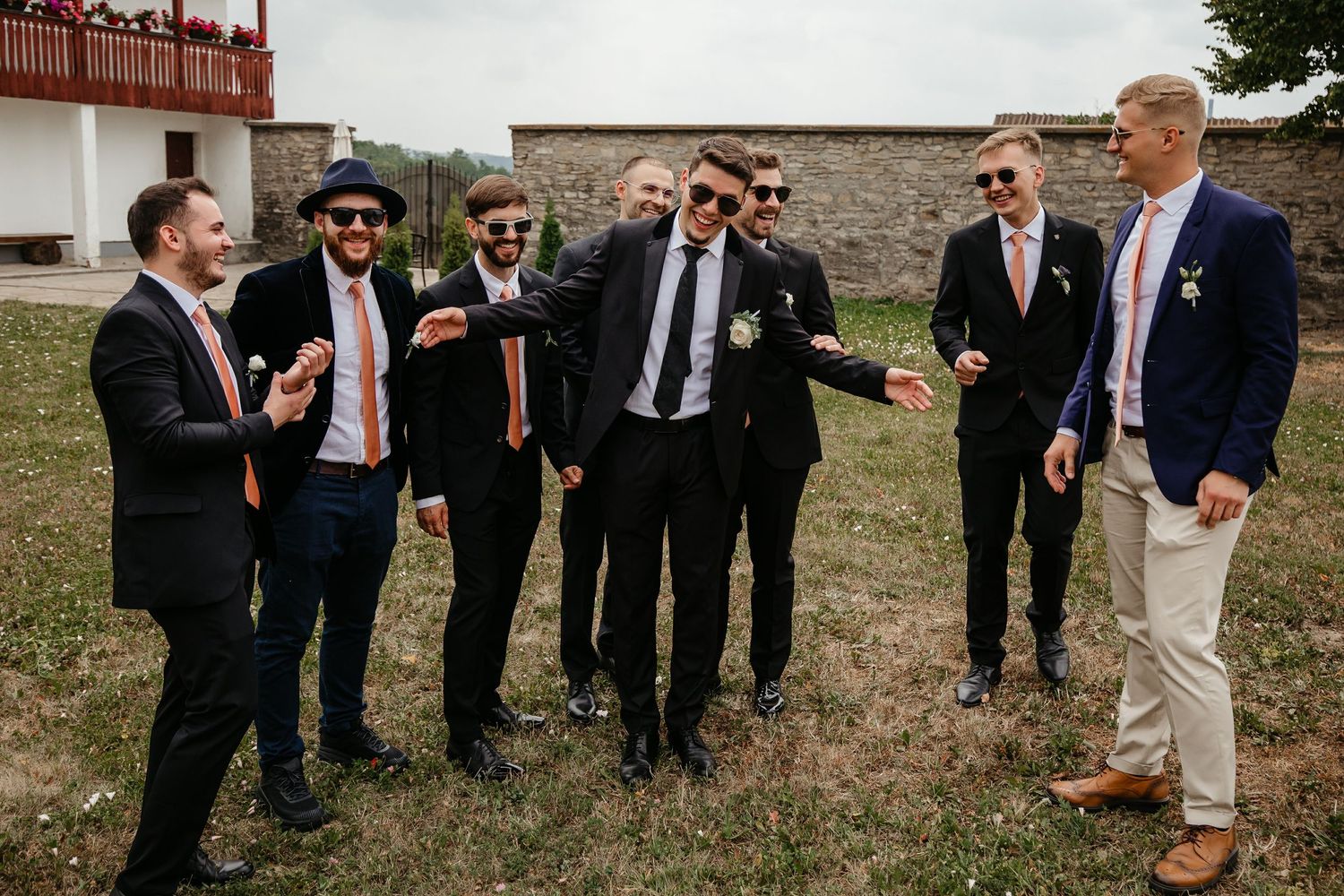 Groomsmen in dark suits and sunglasses laughing together outdoors on a sunny wedding day celebration.