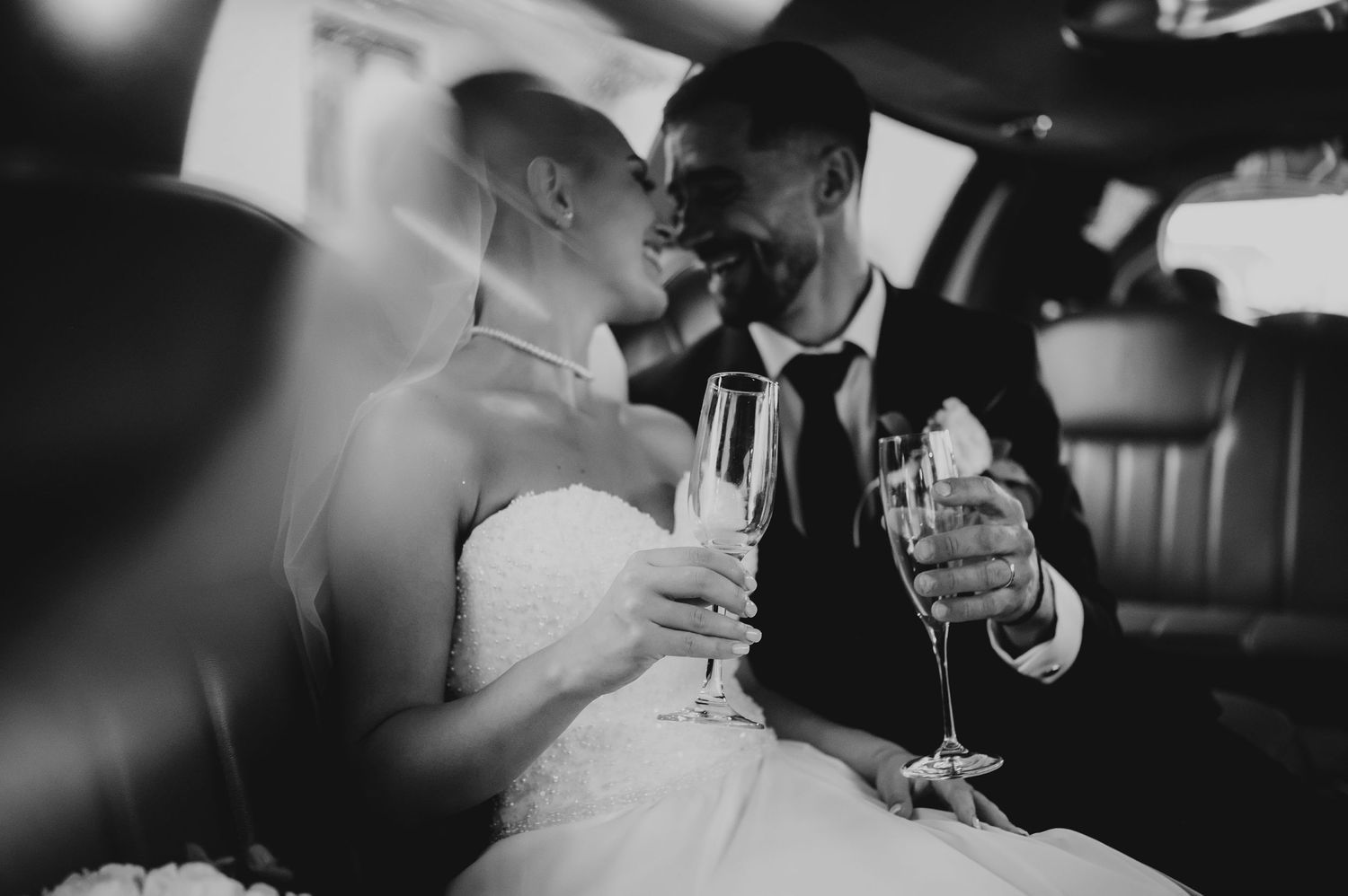 Black and white romantic photo of newlyweds sharing a toast with champagne in a limousine.