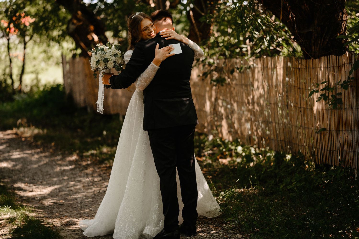 Bride and groom sharing first look embrace outdoors surrounded by lush greenery.