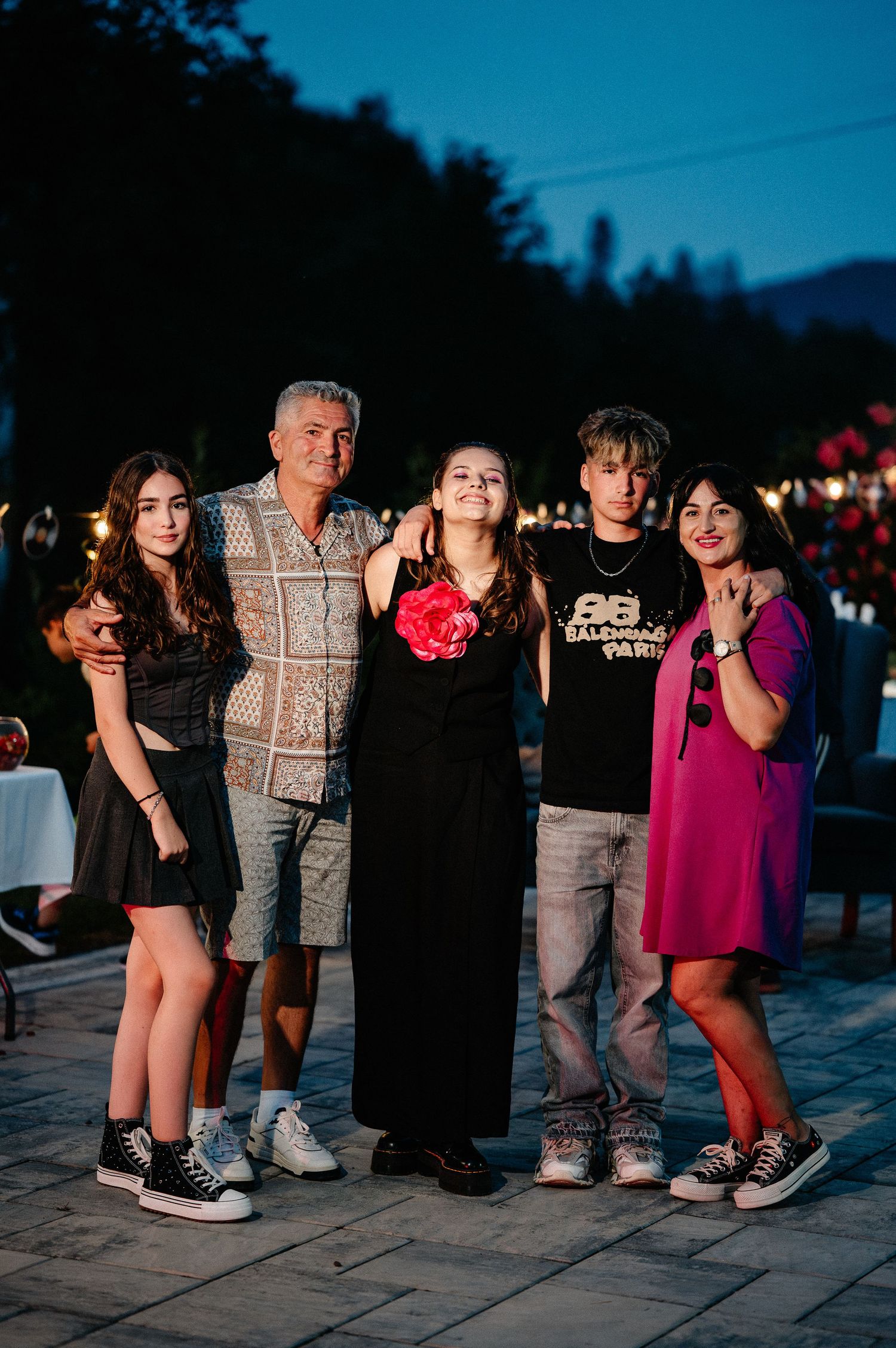 Family of five posing together at a festive outdoor evening celebration with lights.