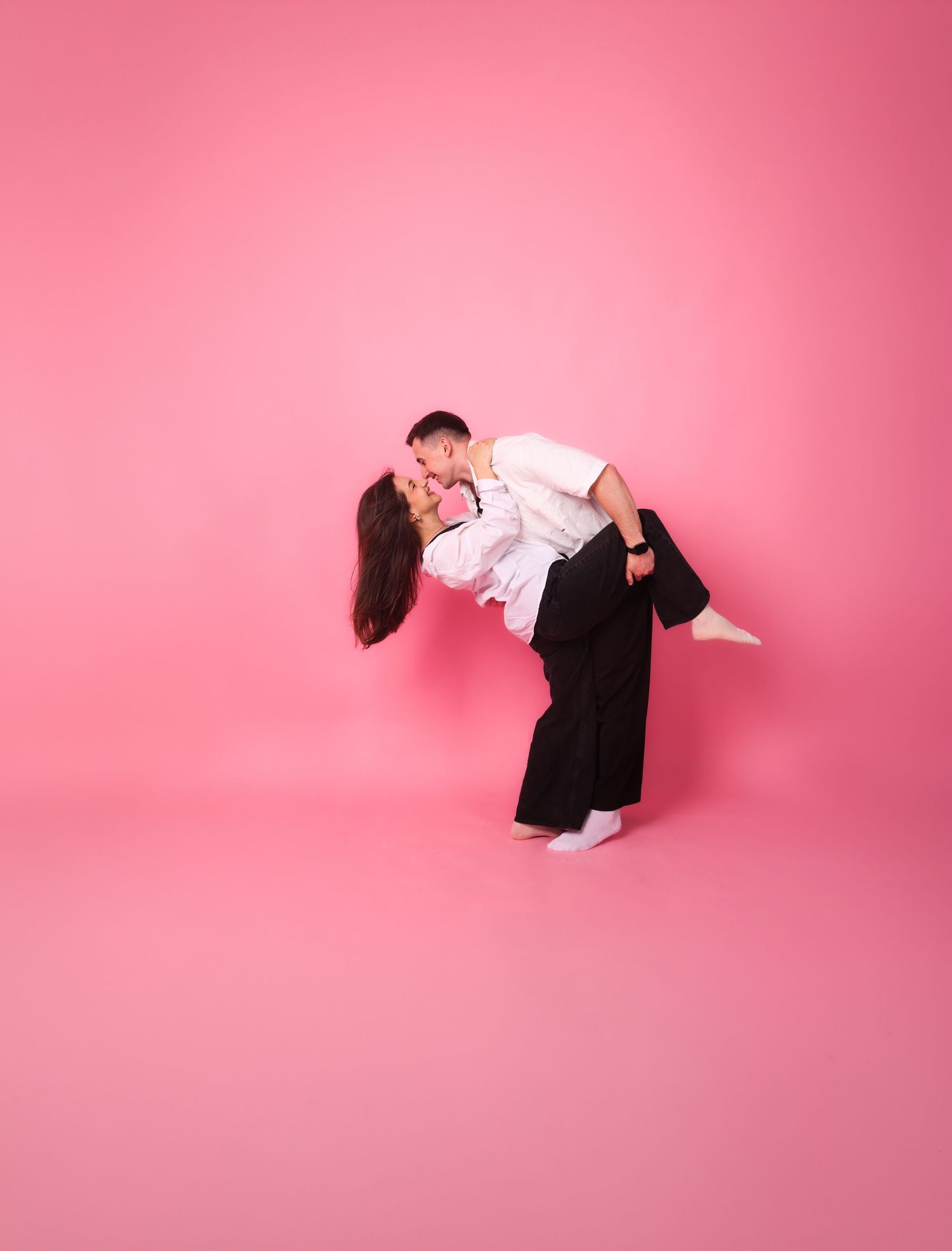 A couple shares a romantic dip kiss against a vibrant pink studio background.