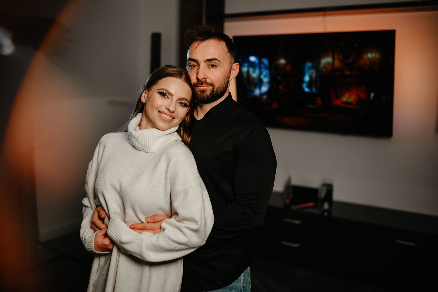Couple posing together in a cozy living room, woman in white sweater, man in black.