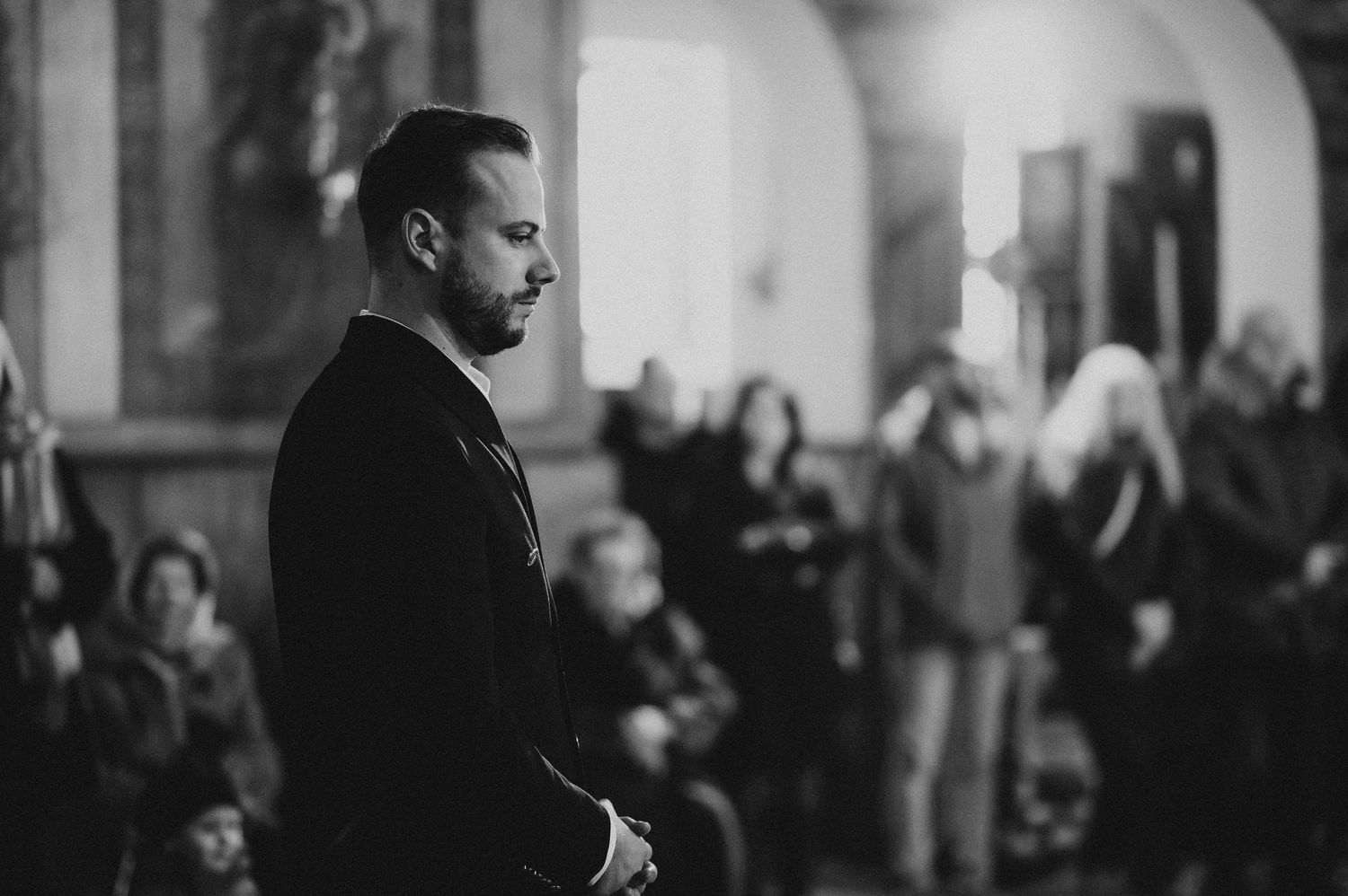 Black and white portrait of man in suit standing solemnly during church baptism ceremony.