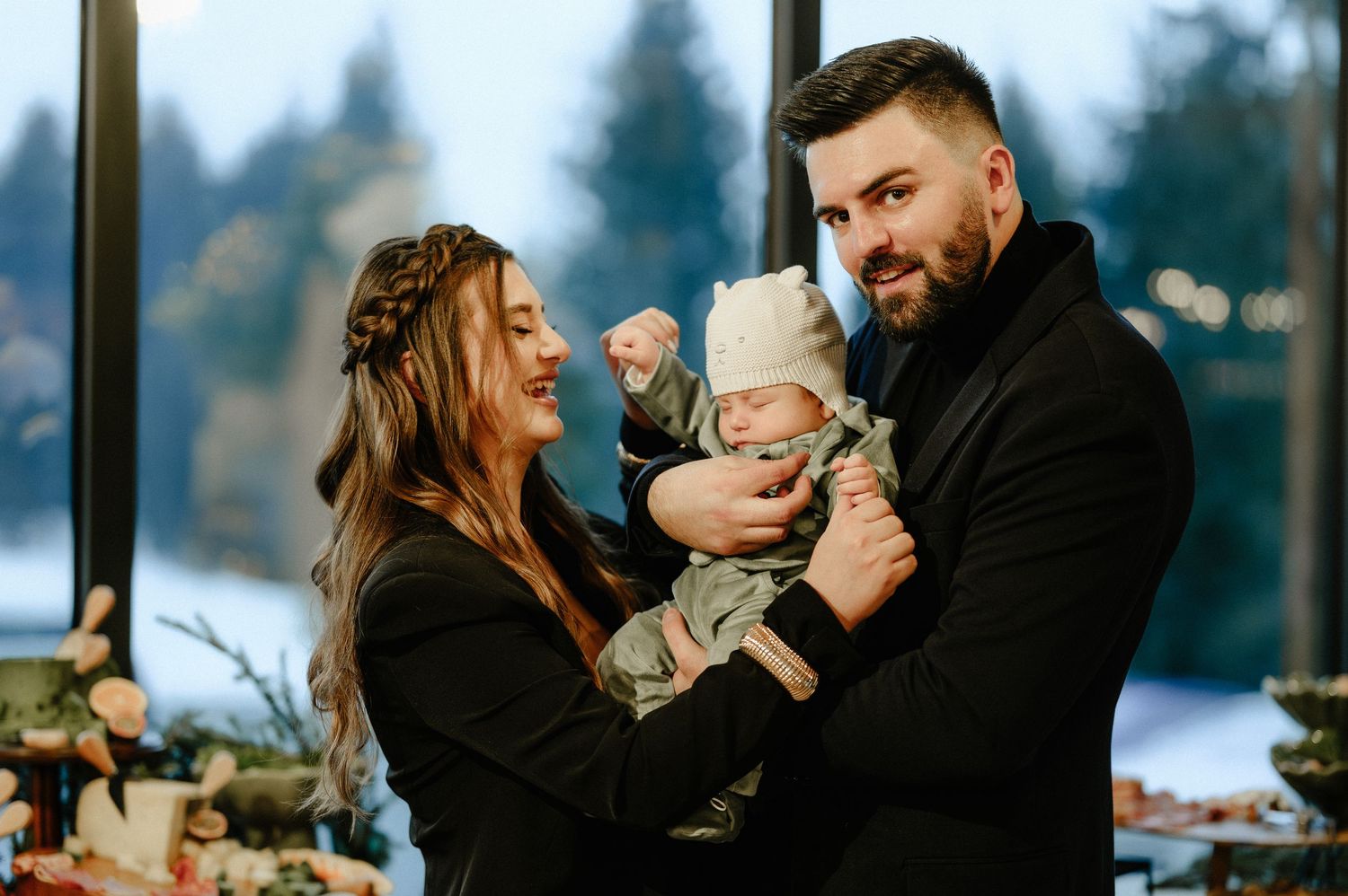 Happy parents in black outfits smiling at their newborn baby at a woodland-themed christening celebration.
