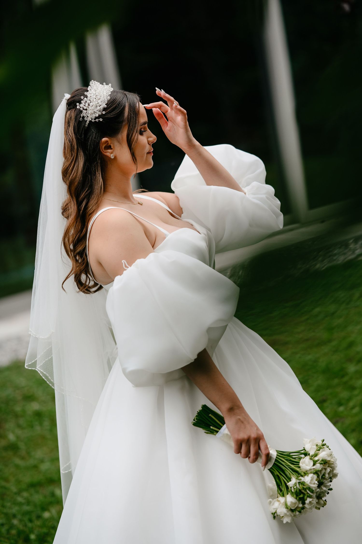 Elegant bride in white ballgown with puff sleeves holds bouquet outdoors.