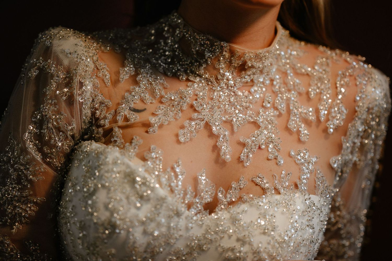 Close-up of bride wearing stunning beaded lace wedding gown with intricate crystal embellishments.