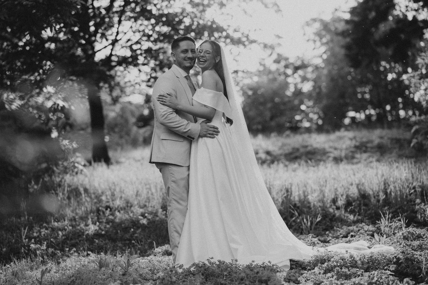 Black and white photo of bride and groom embracing in a lush garden setting on their wedding day.