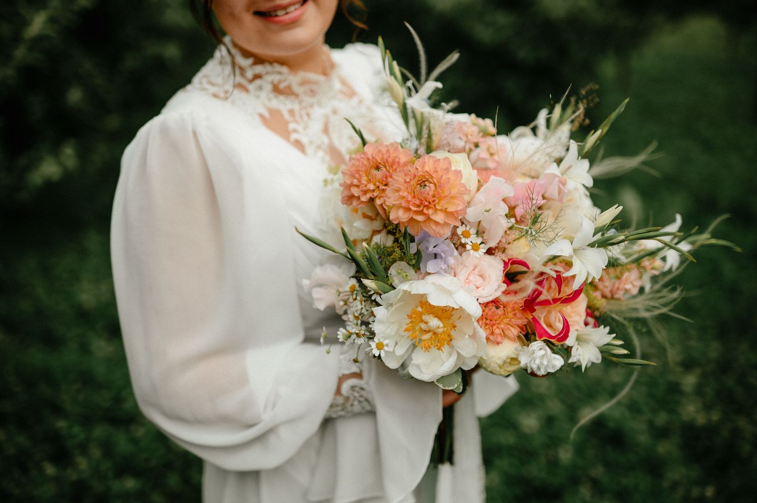 Close-up of bride holding lush peach and pink wedding bouquet.