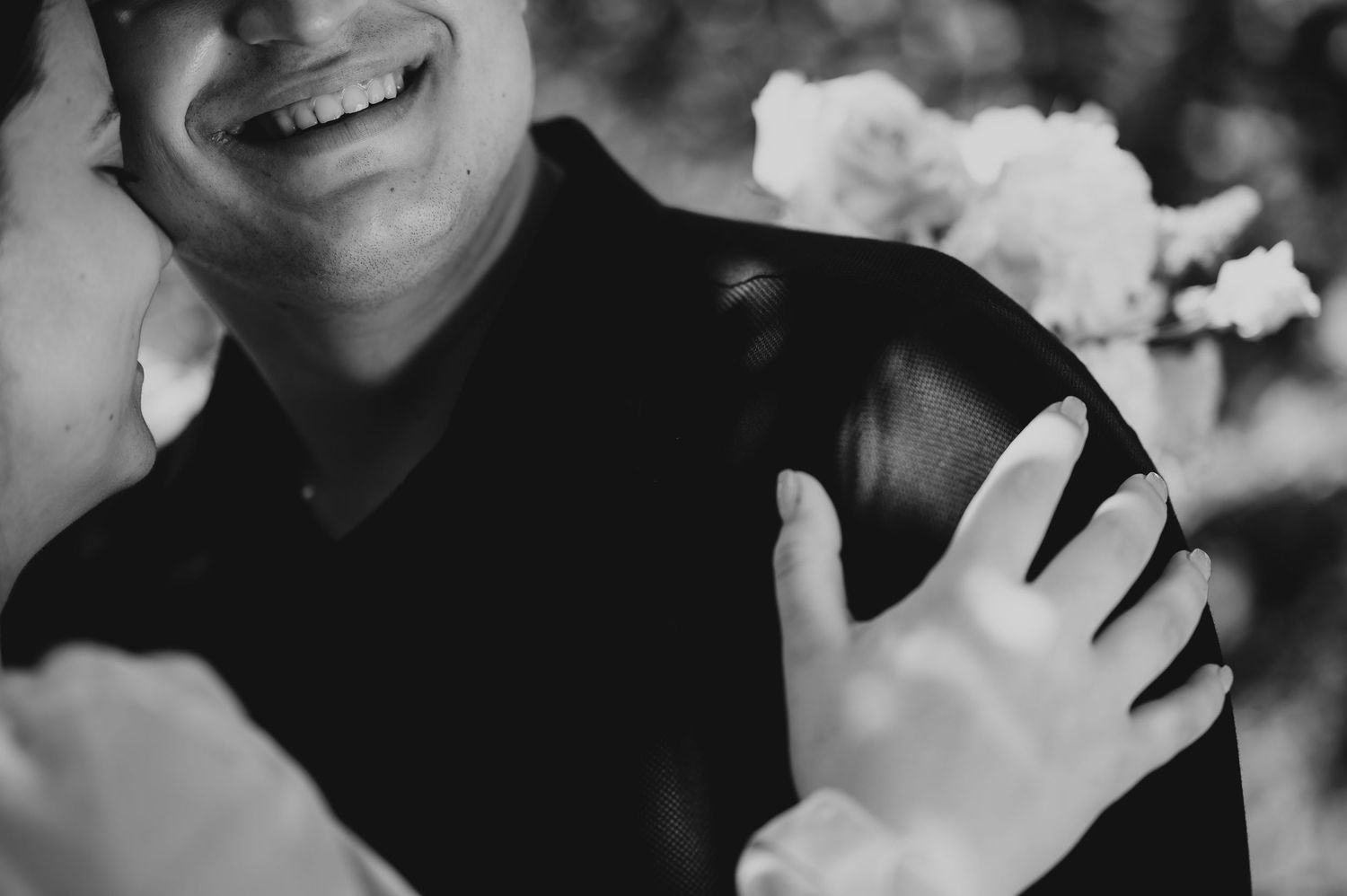 Black and white close-up of a smiling groom embracing his partner holding a white bouquet.