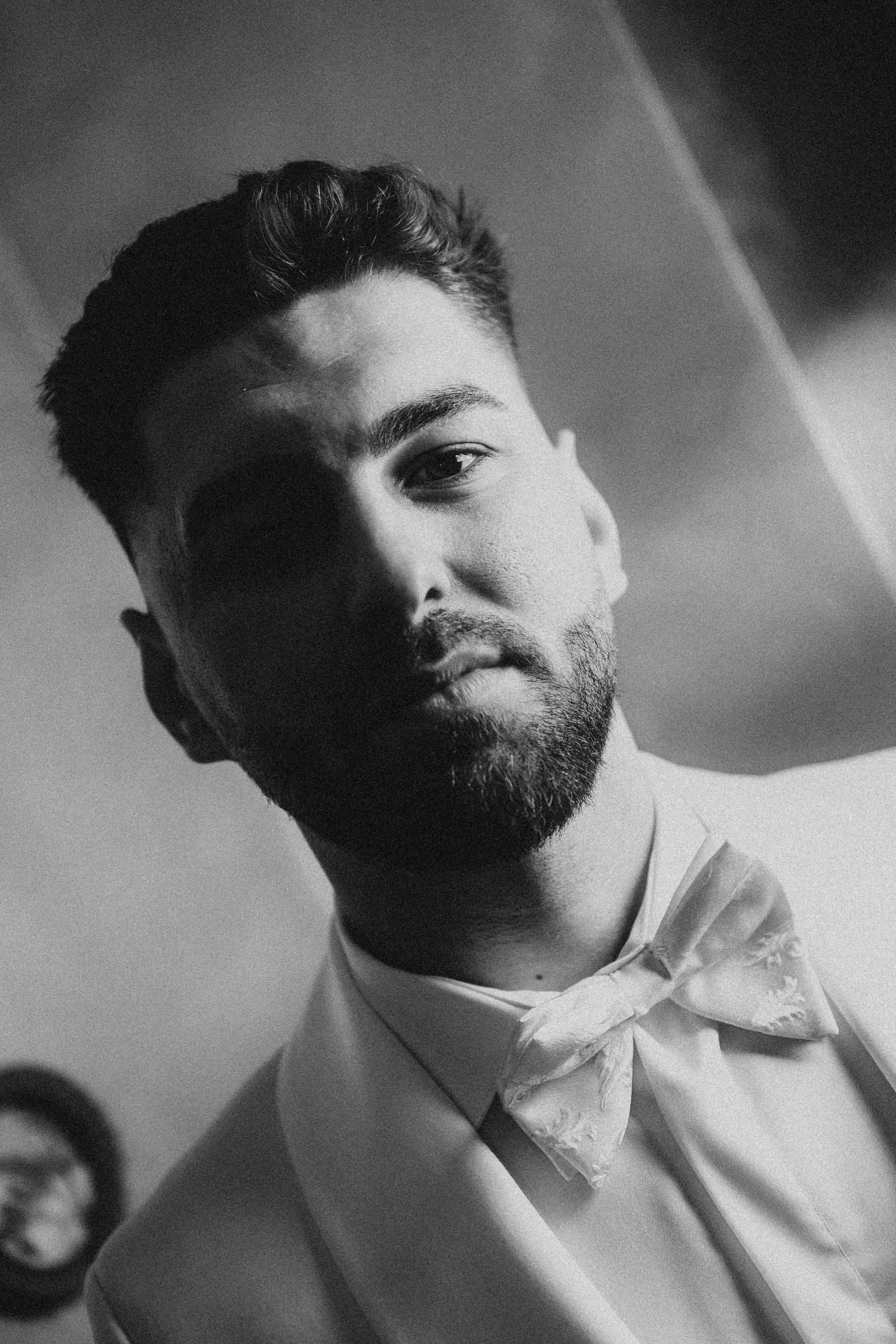 Black and white portrait of a bearded young man wearing a bow tie and suit, looking confidently at the camera.