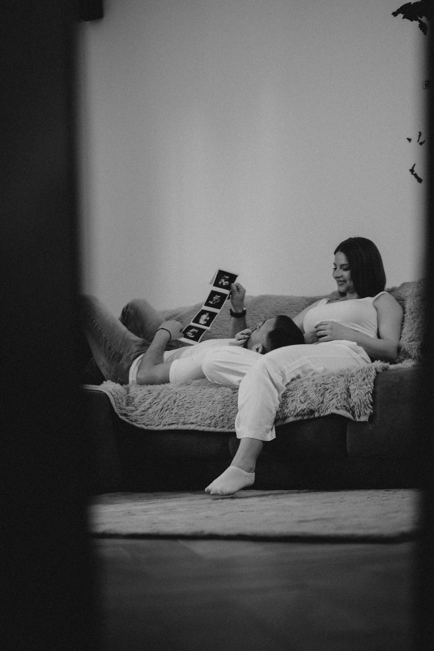 Black and white photo of pregnant couple on couch reviewing ultrasound images together.