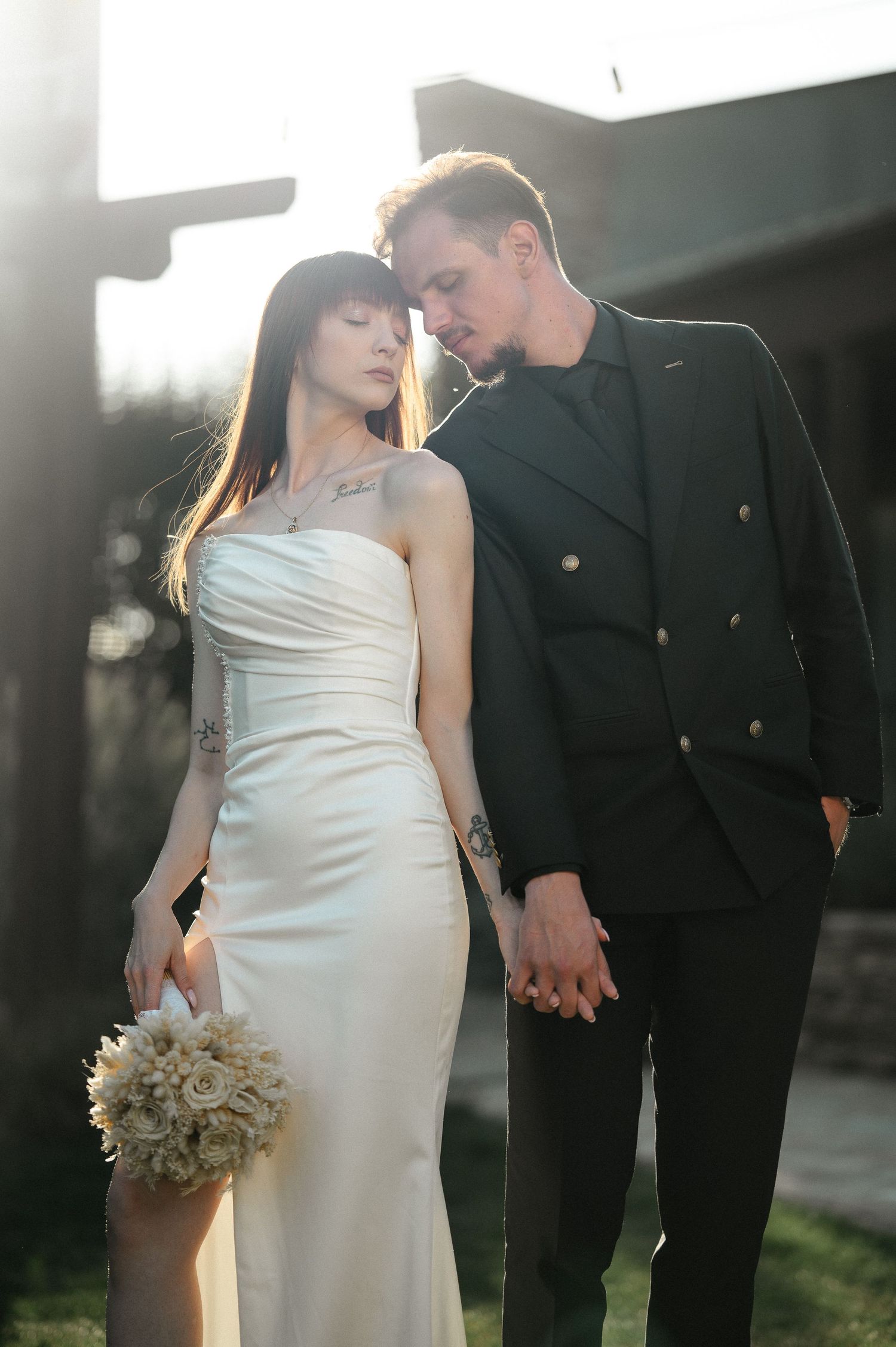 Bride and groom sharing an intimate moment in golden backlight, she in white gown holding a bouquet.