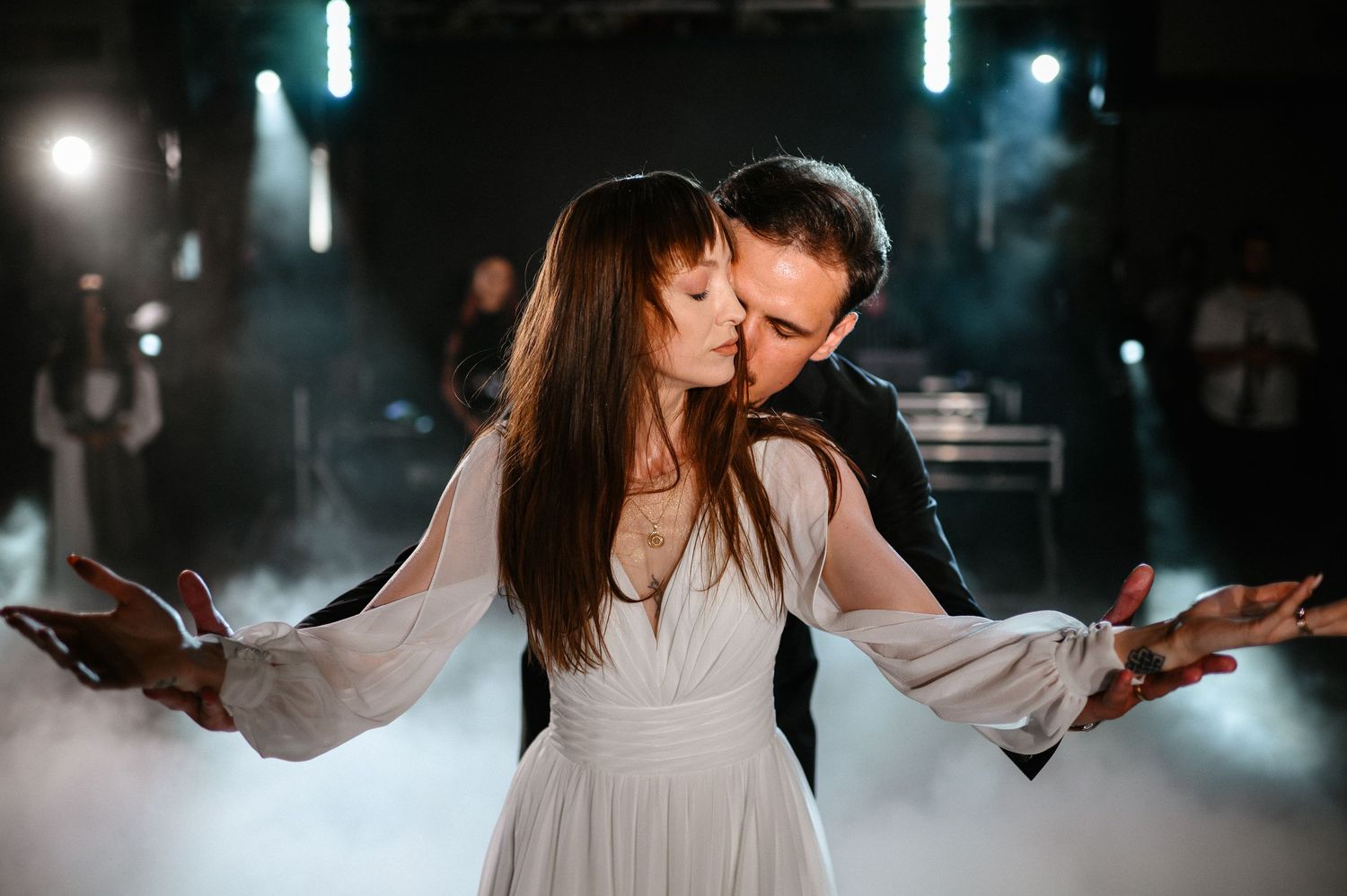 Bride and groom share passionate kiss during first dance surrounded by romantic fog and stage lights.