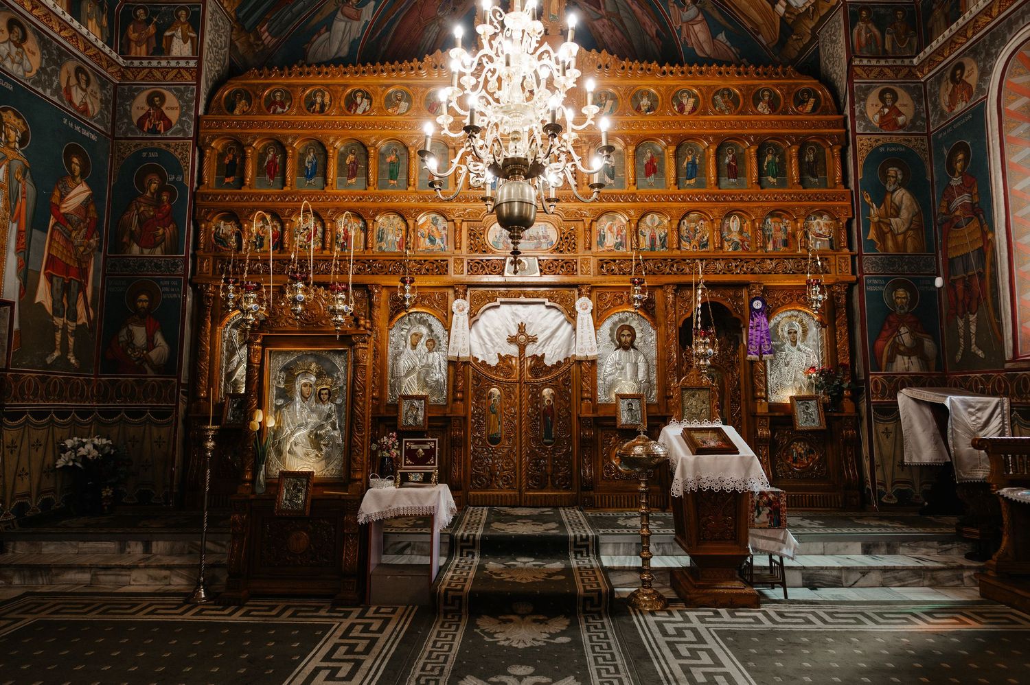 Ornate Orthodox church interior featuring golden iconostasis, chandelier, and colorful religious murals.