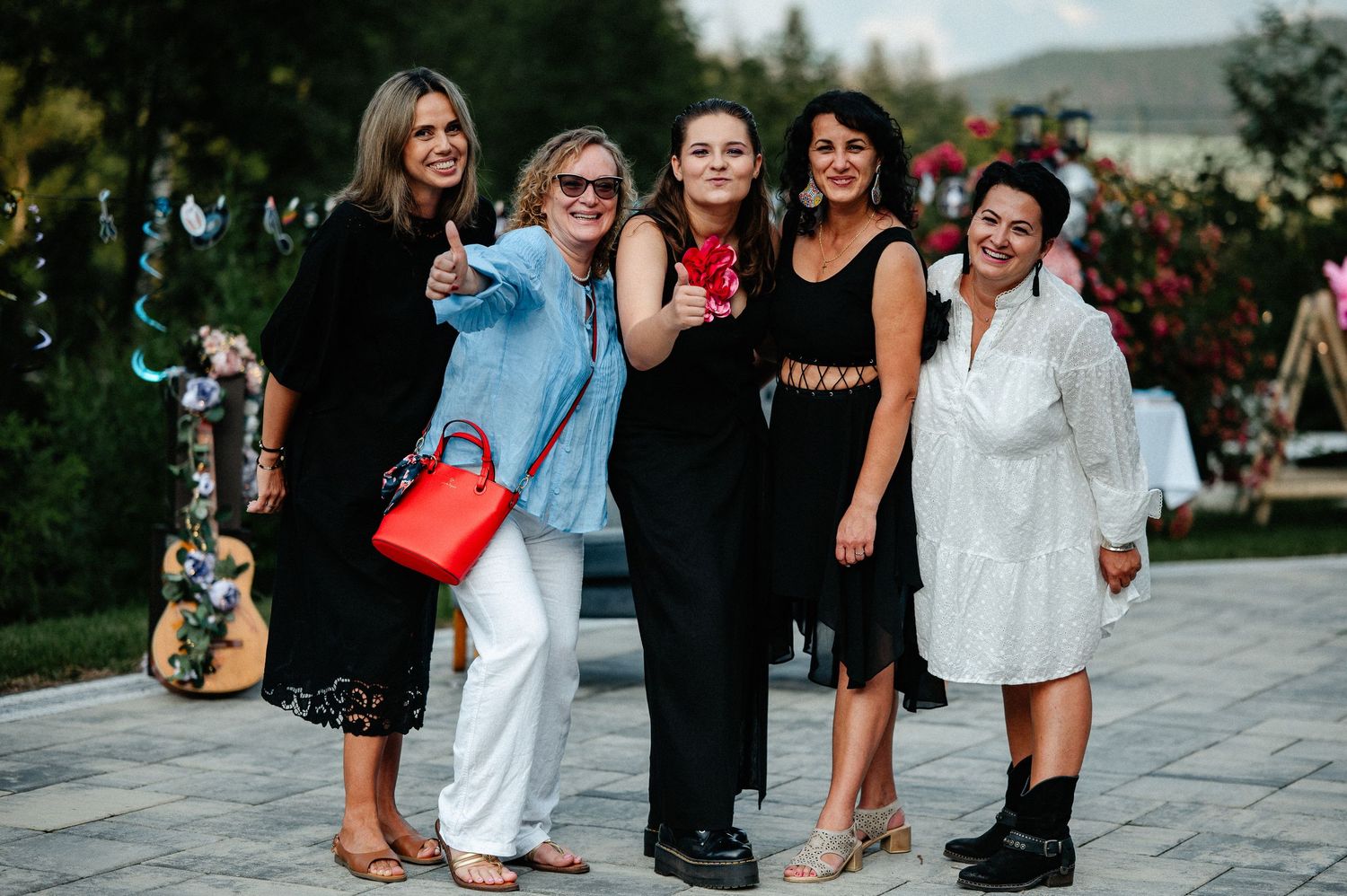 Group of five women smiling together at an outdoor garden party celebration.