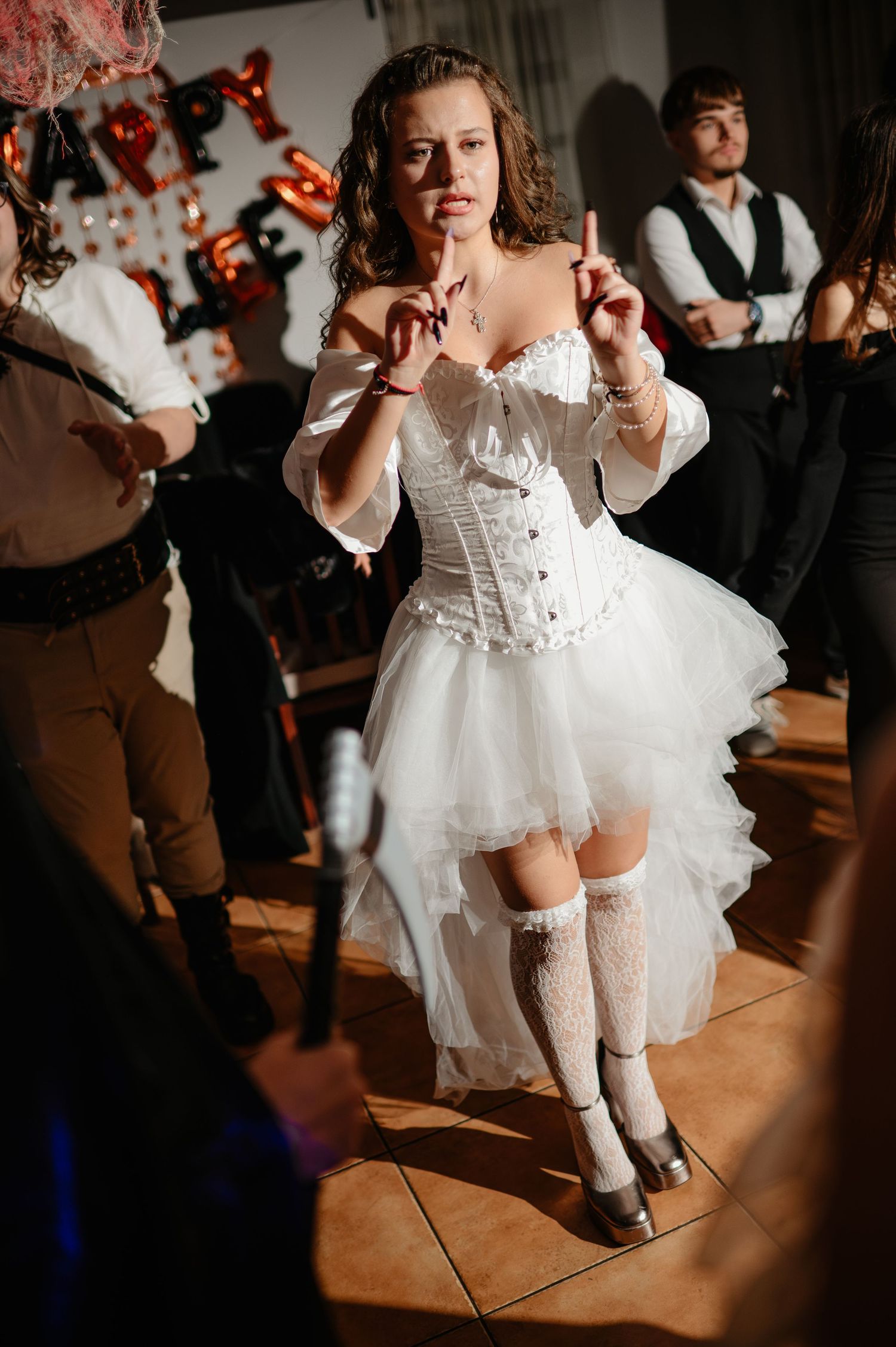 Woman in white corset and tutu skirt dances energetically at Halloween costume party indoors.
