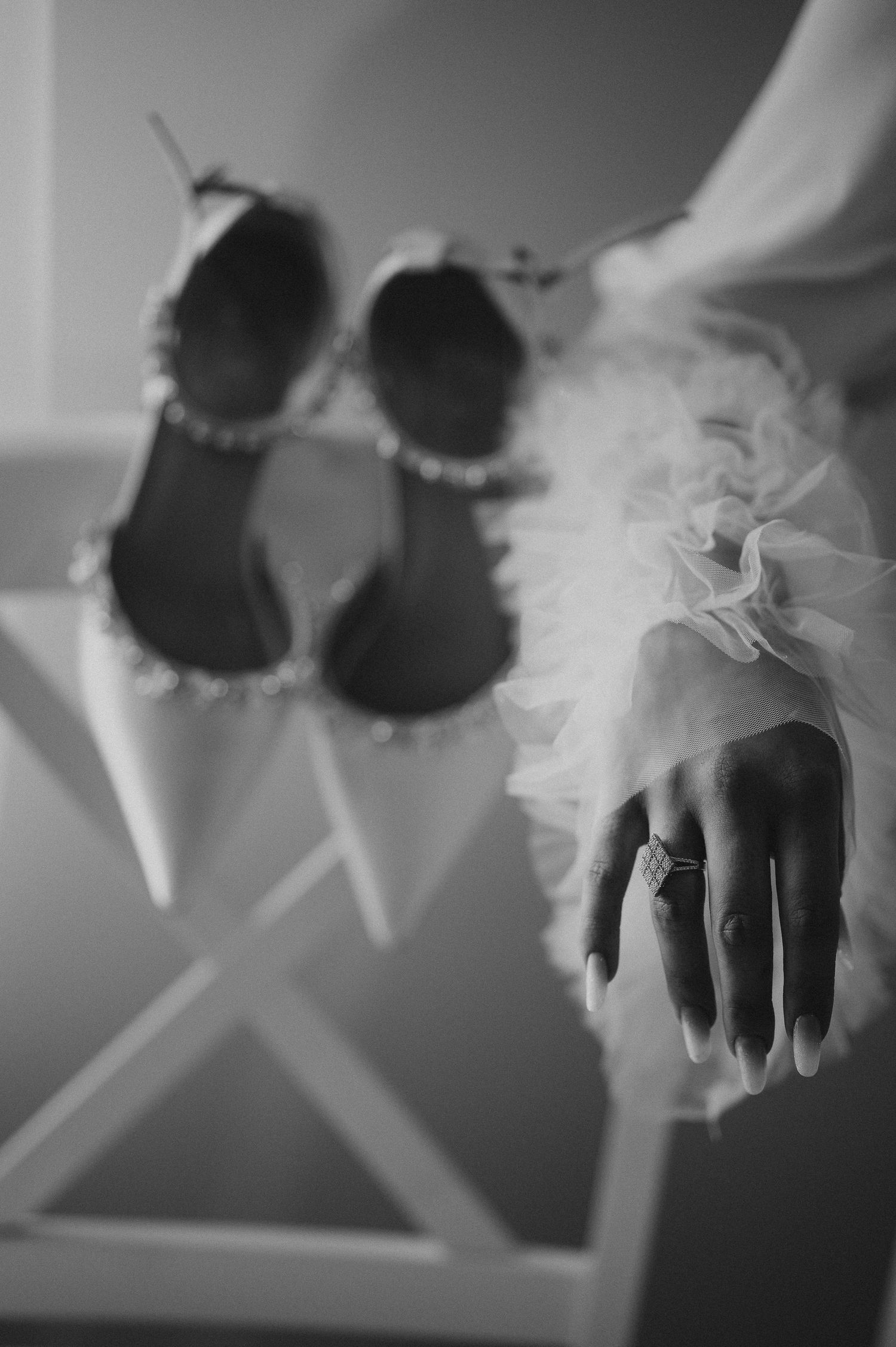 Black and white close-up of bridal shoes and a hand with rings in a ruffled sleeve.