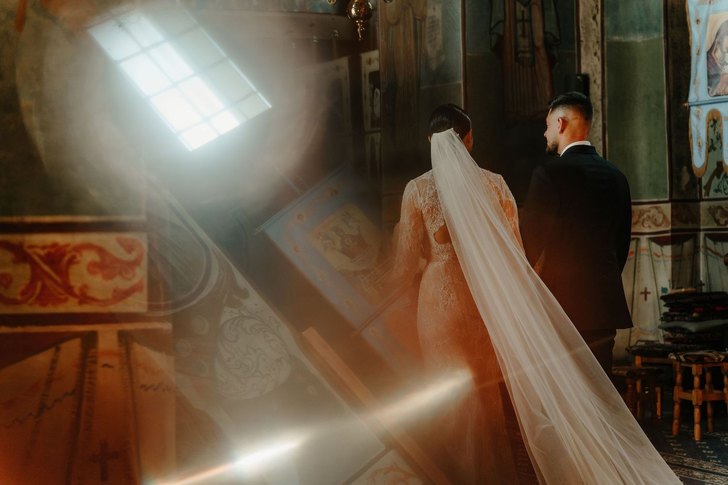 Bride and groom walking toward light streaming through church windows during their Orthodox wedding ceremony.