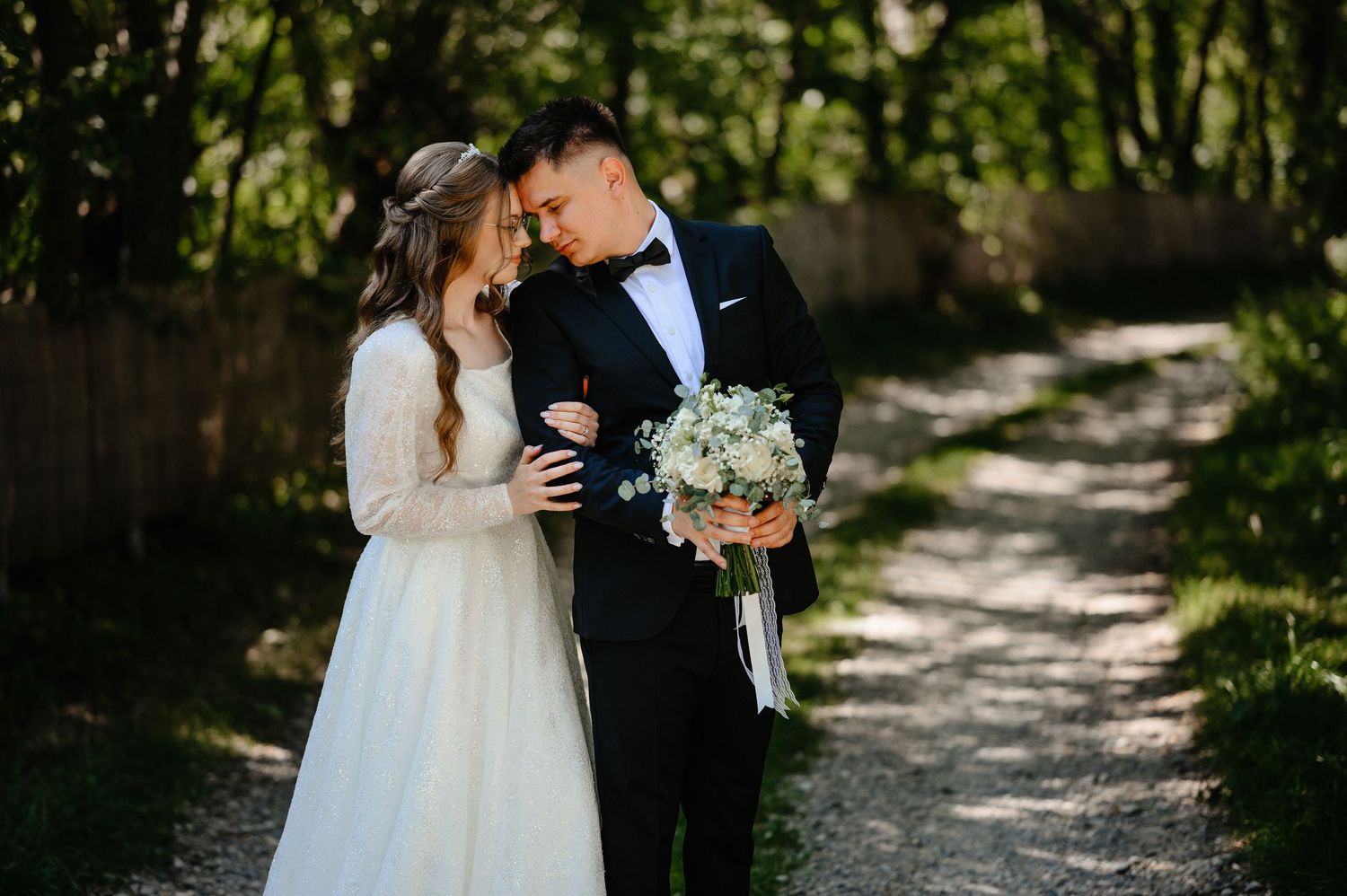 Romantic bride and groom embracing on a scenic garden path with white bouquet.