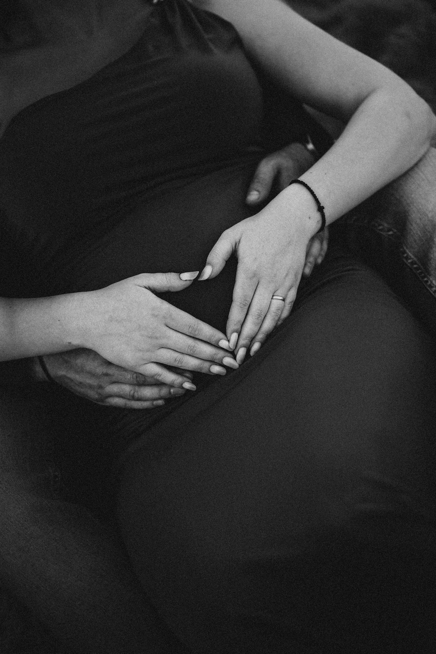 Close-up black and white photo of couple placing hands together on pregnant belly.