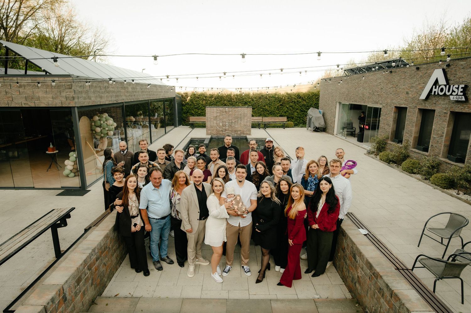 Large group of smiling people posing together on steps outside the House venue at dusk.