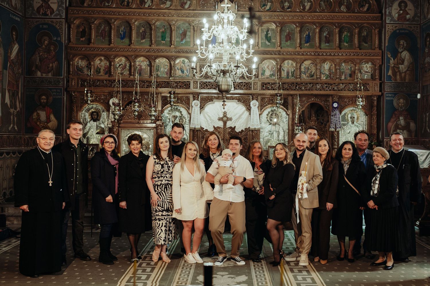 Large family group portrait inside an Orthodox church following a baby baptism celebration.