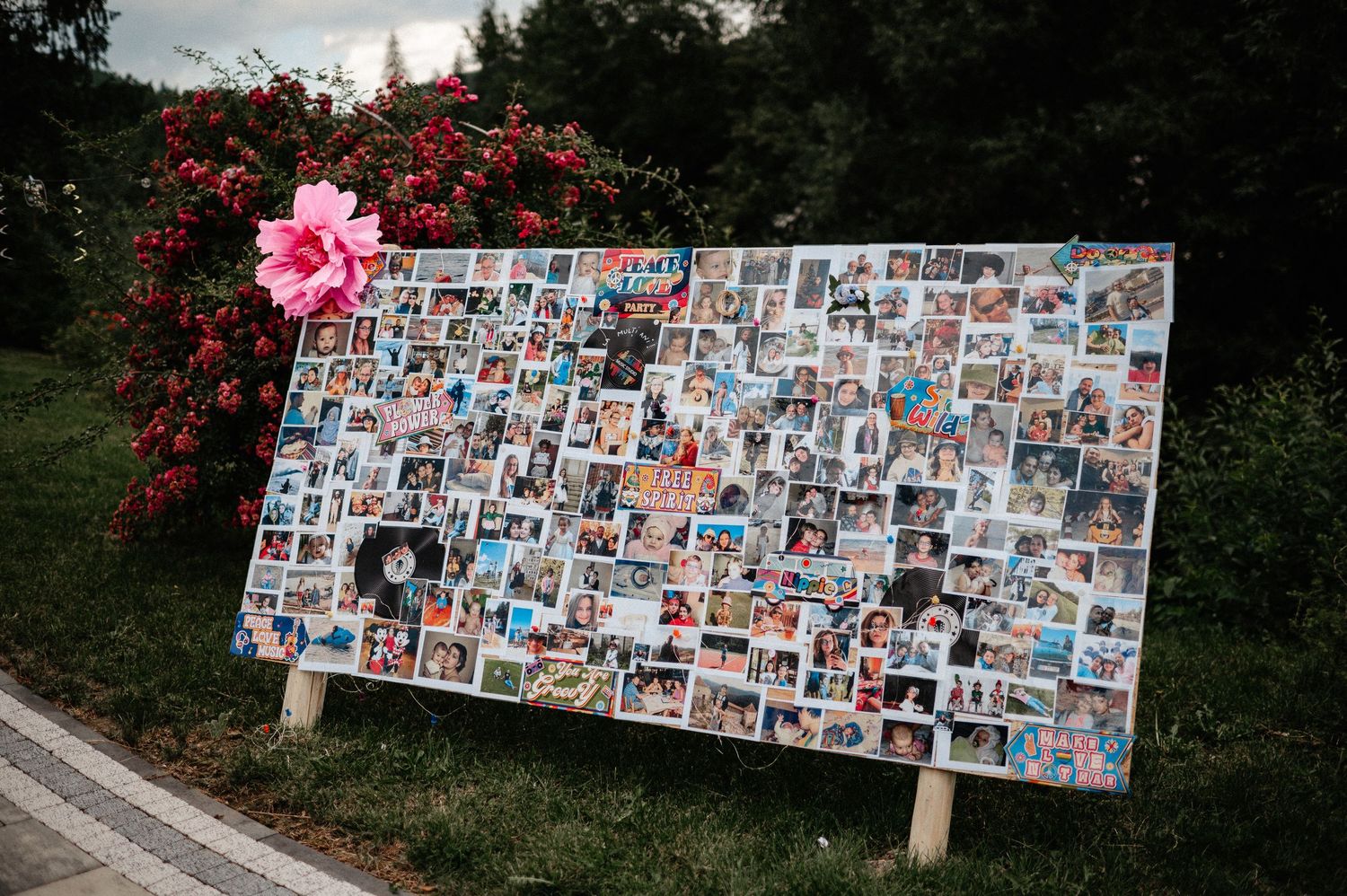Large photo collage display board decorated with a pink flower, showcasing memories at an outdoor party.