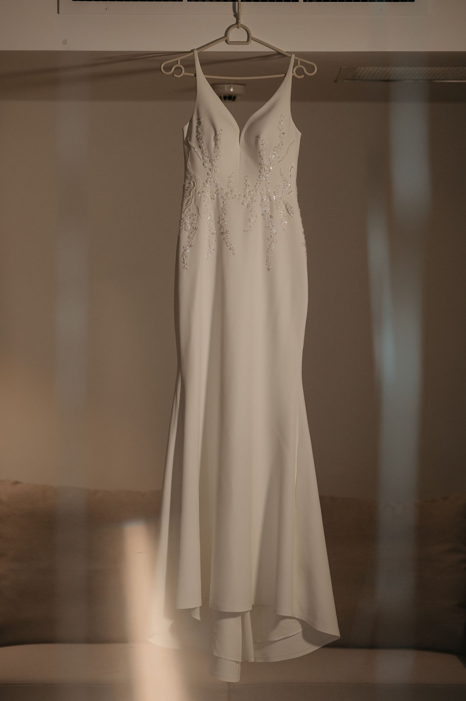 Elegant white mermaid wedding dress with lace bodice hanging on hanger in soft light.