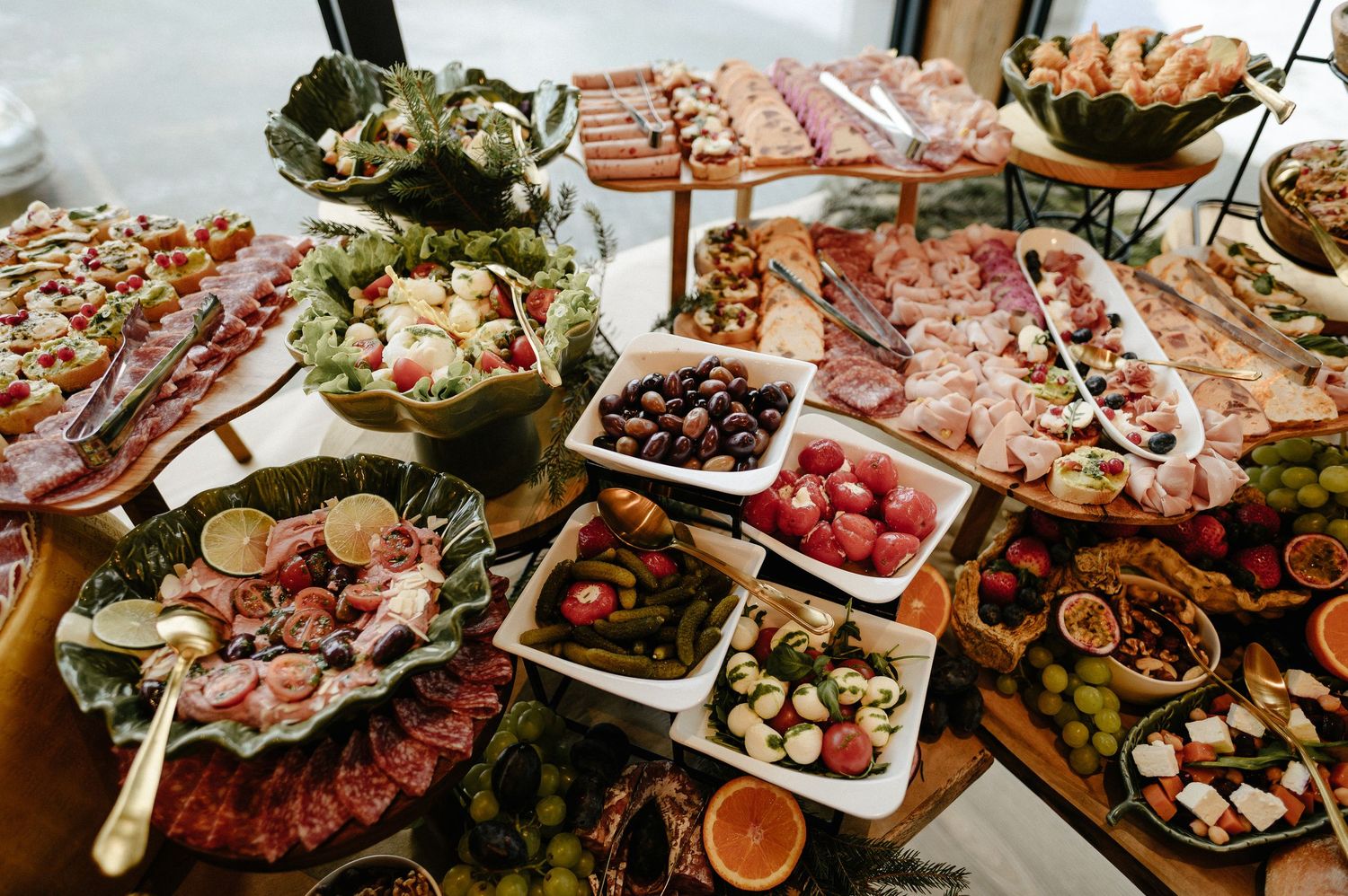 Elaborate grazing table spread with charcuterie, fresh fruits, vegetables, and gourmet appetizers arranged on tiered wooden boards.