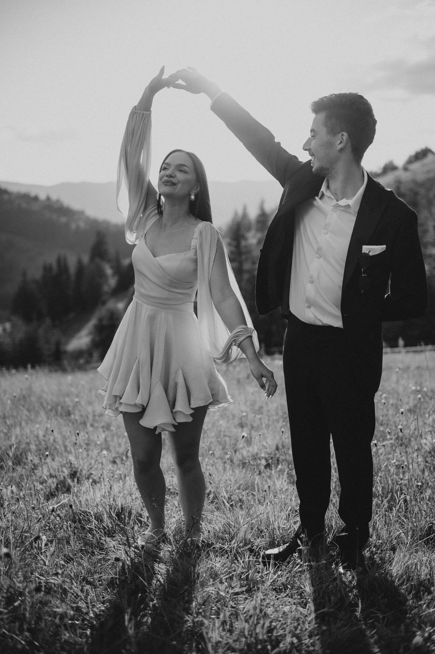 Black and white photo of couple dancing in a mountain field, man spinning woman in a short dress.