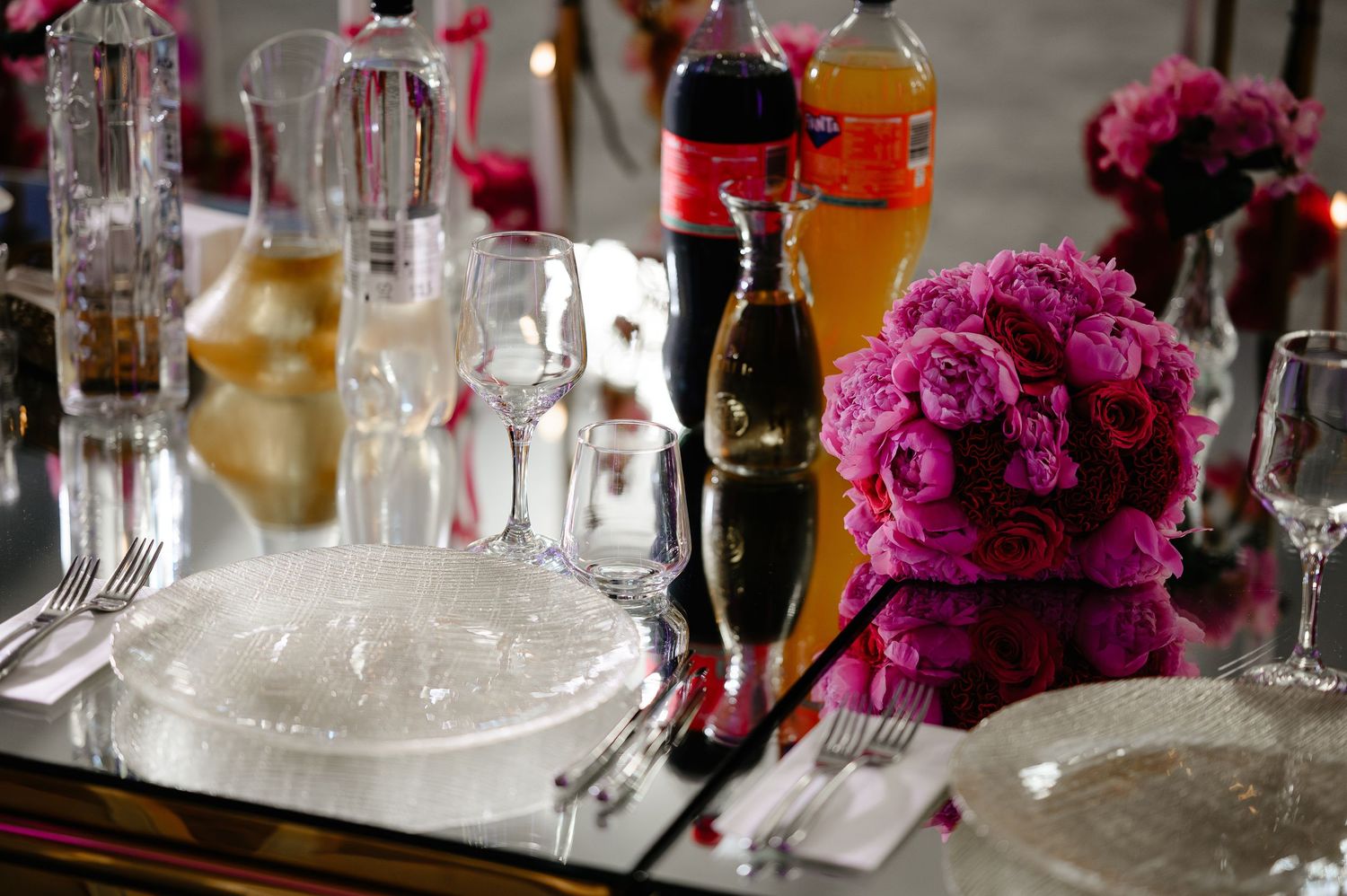 Mirrored wedding table with pink rose centerpiece, glassware, and beverage bottles.