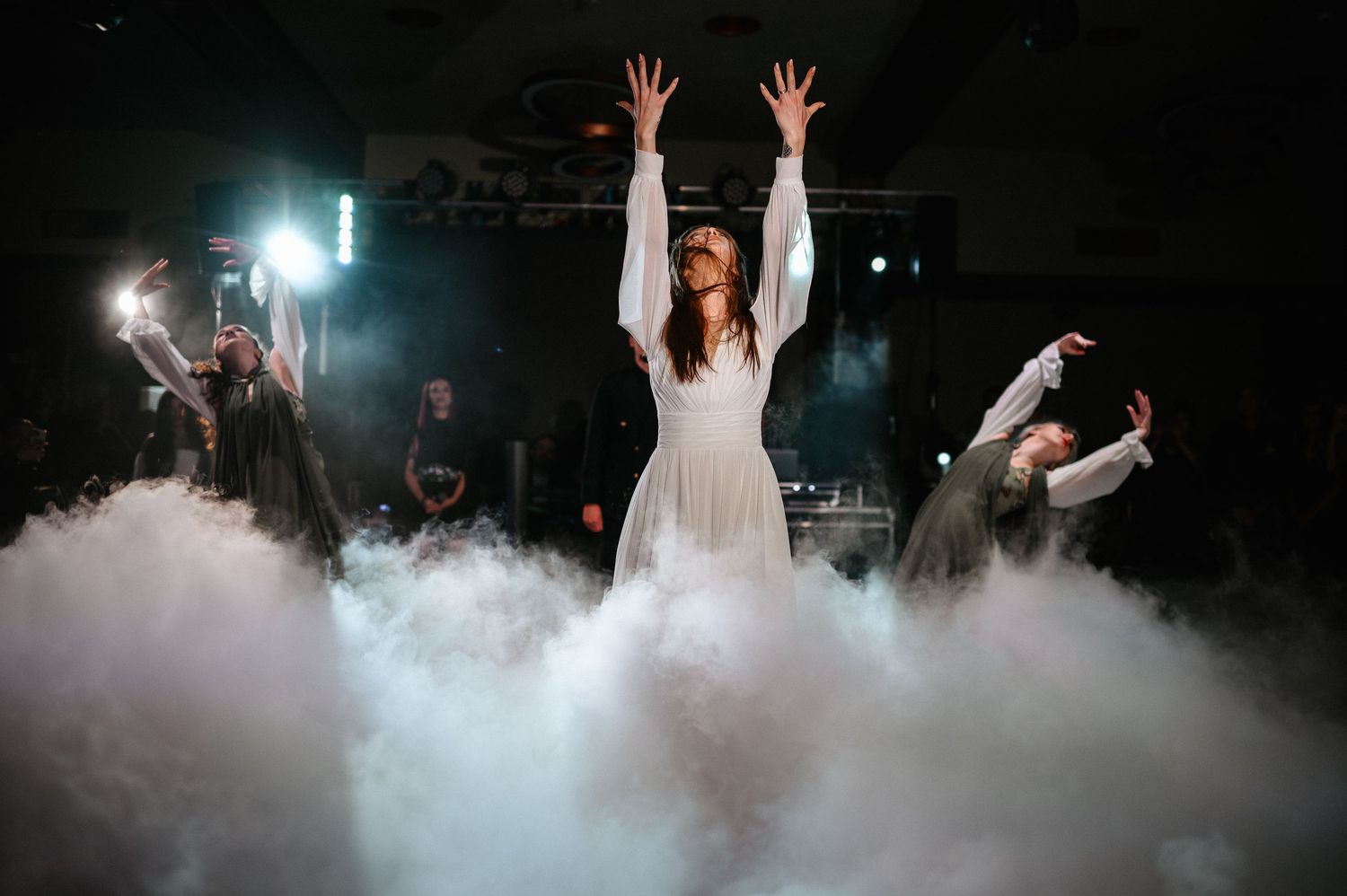 Bride raises arms dramatically during wedding dance performance enveloped in thick white fog on stage.