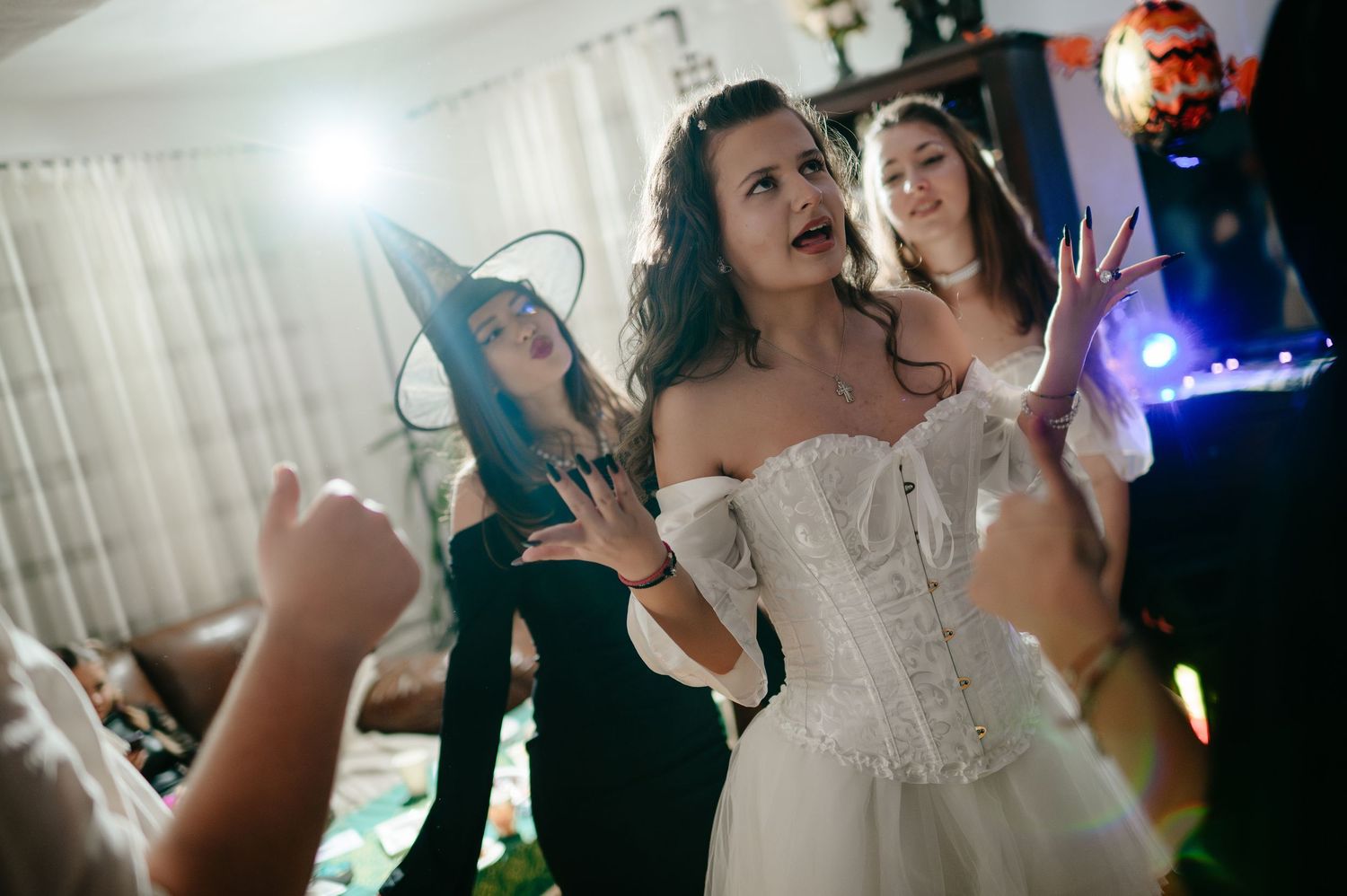 Women in Halloween costumes including witch hat and white corset dance at festive party.