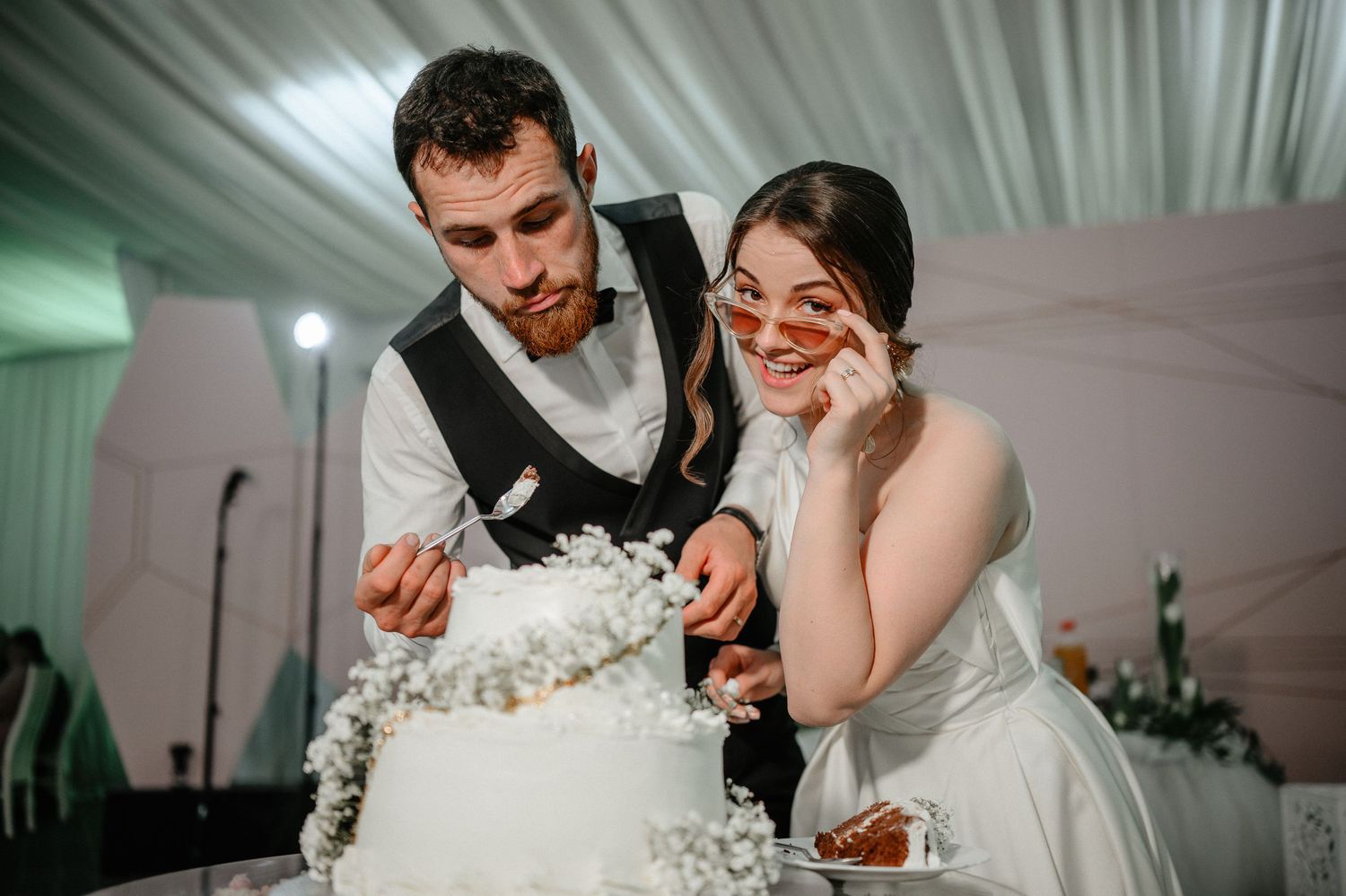 Bride and groom cutting their white wedding cake decorated with baby's breath flowers at reception.