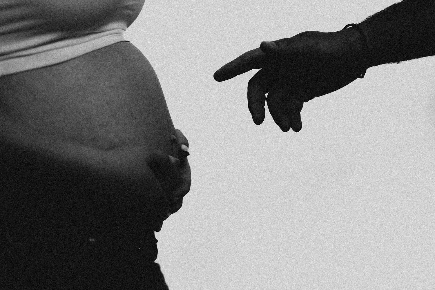 Black and white photo of pregnant woman's belly with a hand pointing at it from the side.